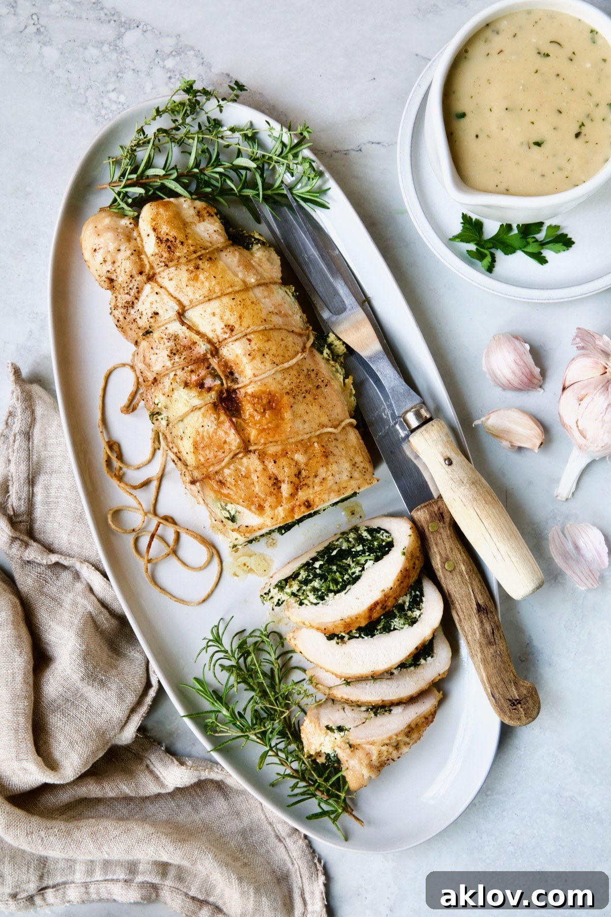 Spinach and Ricotta Stuffed Turkey Breast with Garlic - Herb Sauce presented on a white oval platter with serving utensils, ready for guests.