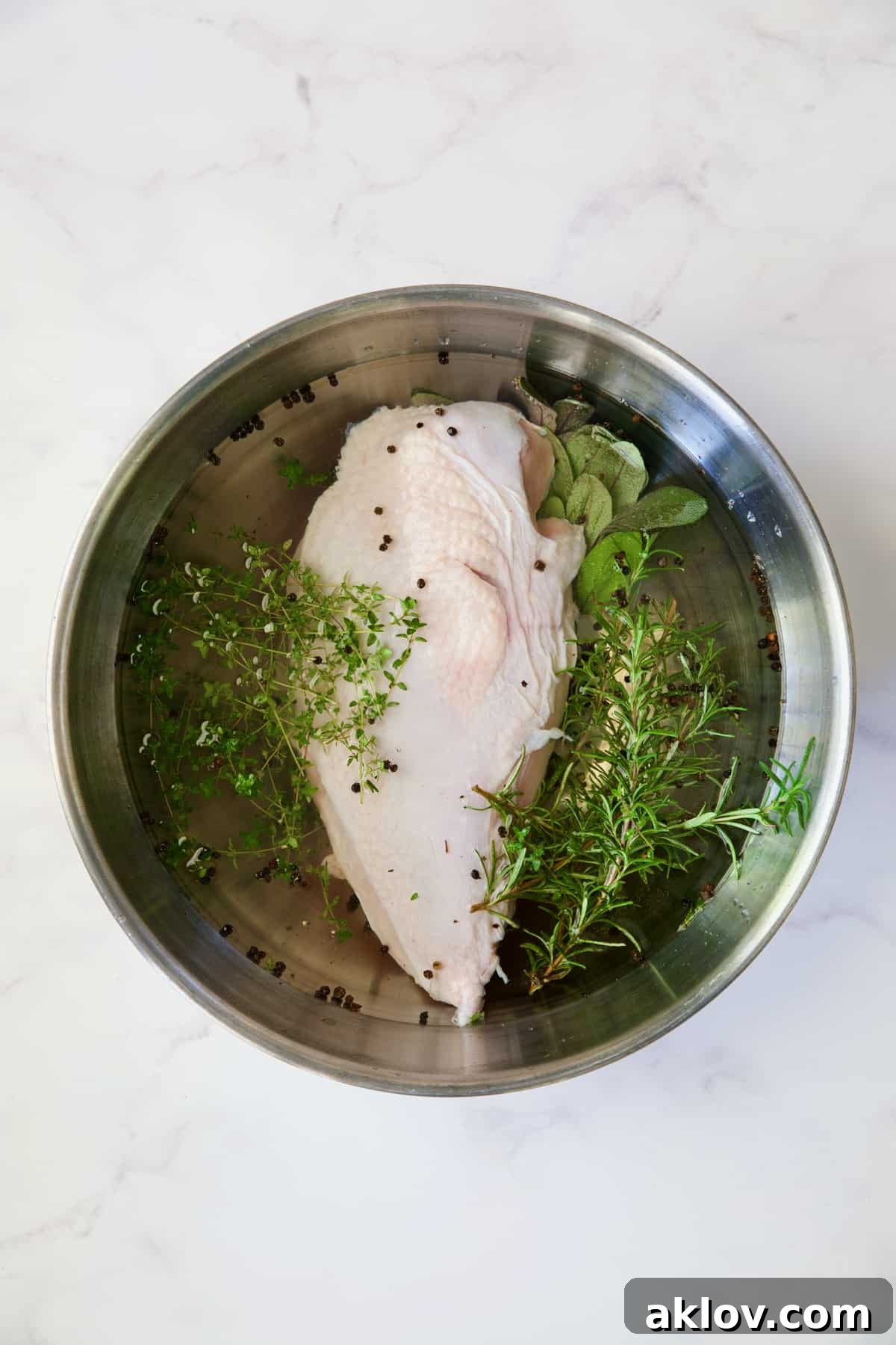 Turkey breast half submerged in an Easy Turkey Brine solution within a stainless steel bowl.