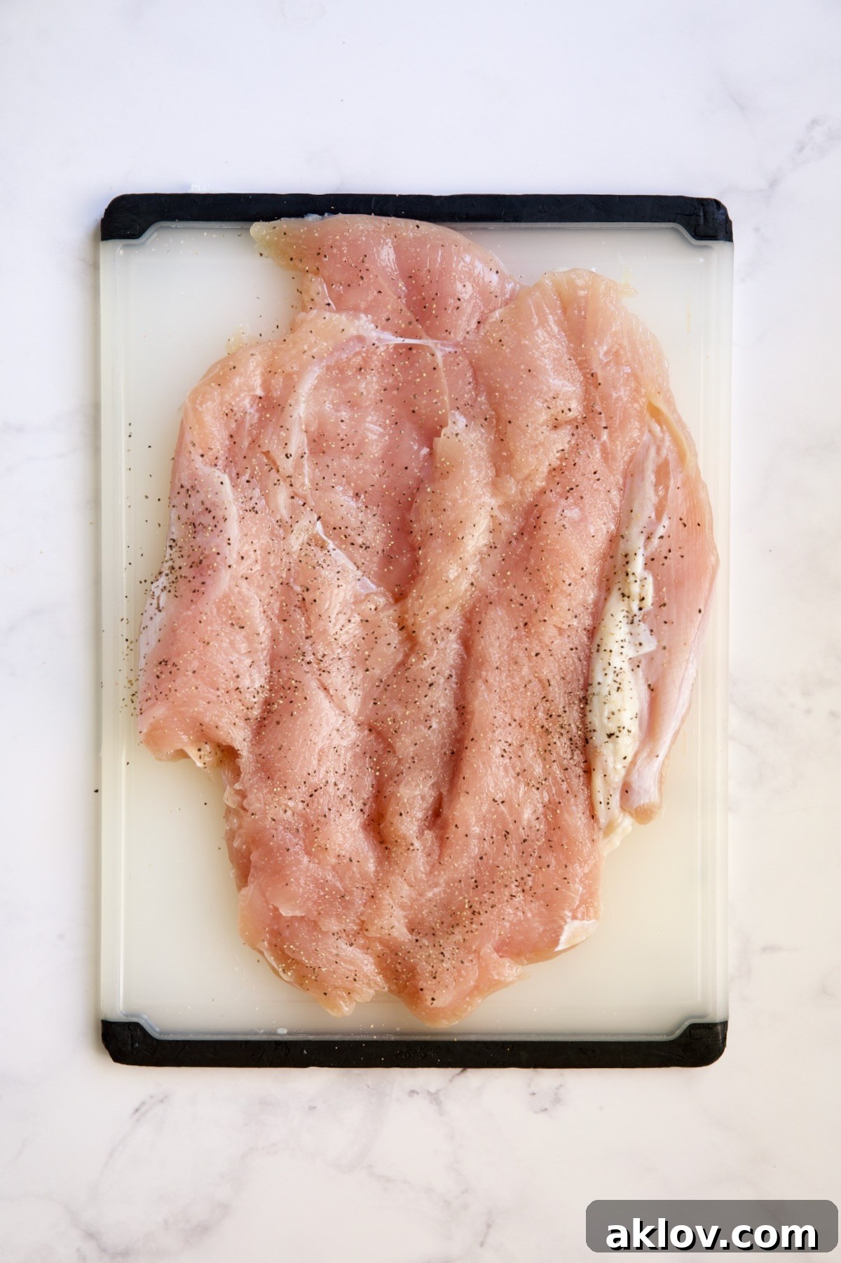 Butterflied turkey breast, flattened and seasoned with salt and pepper, laid out on a white plastic cutting board.
