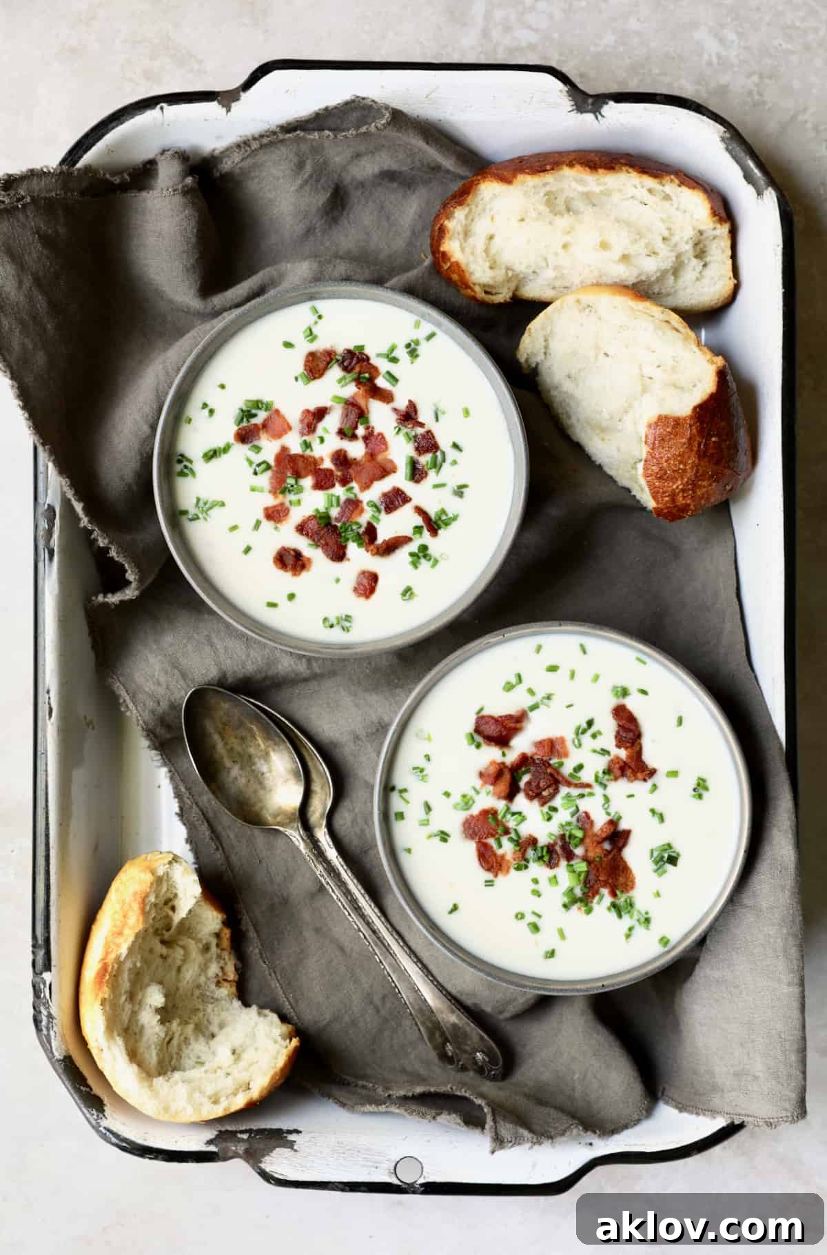 Comforting White Cheddar Potato Leek Soup 2 Photo of two bowls of Potato Leek Soup with White Cheddar on gray napkin in white tray with bread.