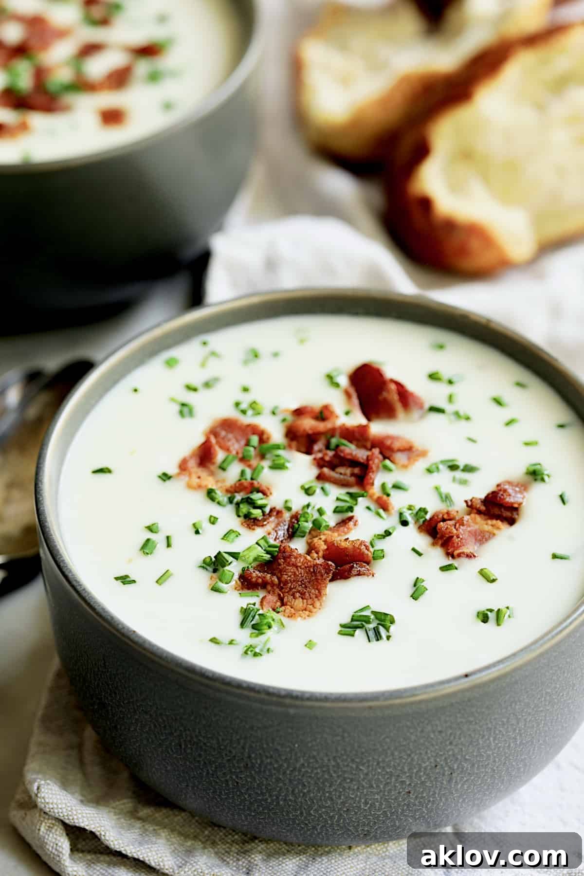 Comforting White Cheddar Potato Leek Soup 12 Close-up photo of Potato and Leek Soup with White Cheddar in gray bowl garnished with bacon and chives.