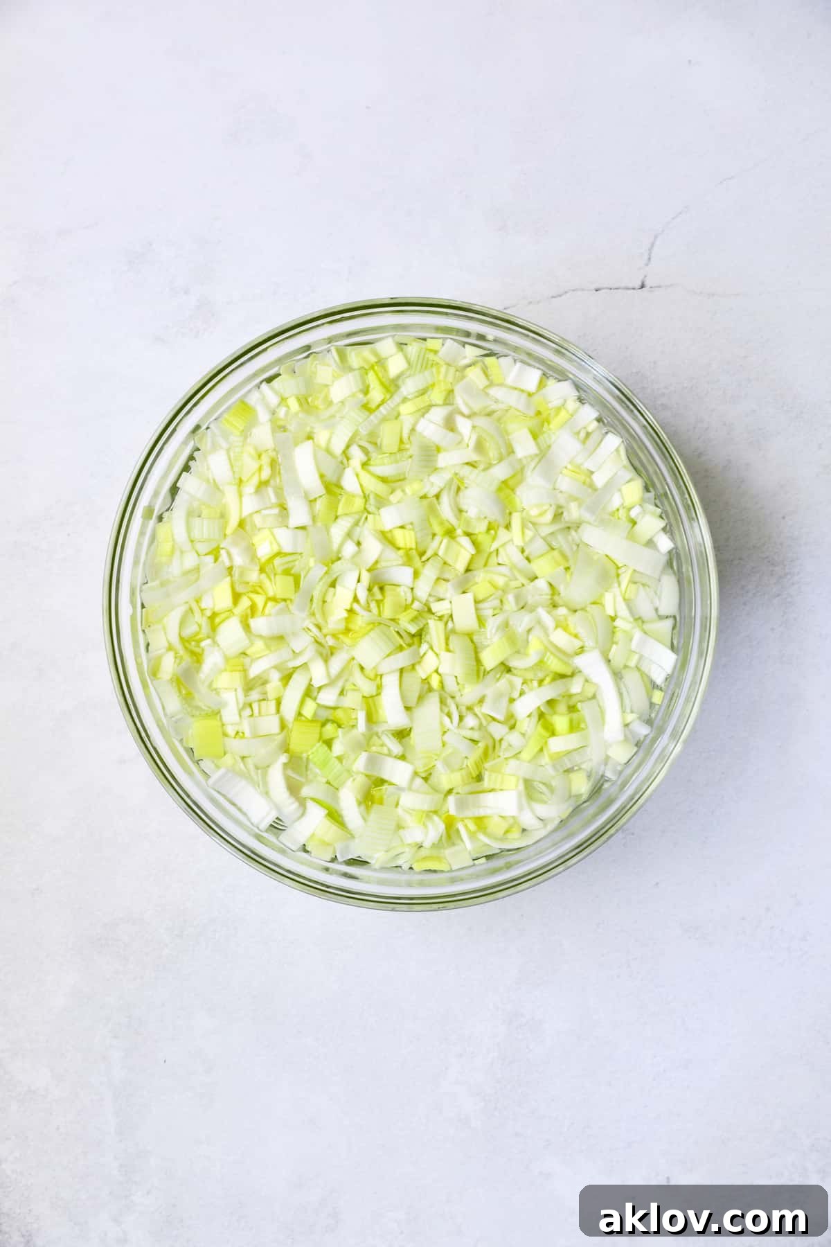 Sliced leeks submerged in a glass bowl filled with clean water, illustrating the proper cleaning method for removing dirt and grit.