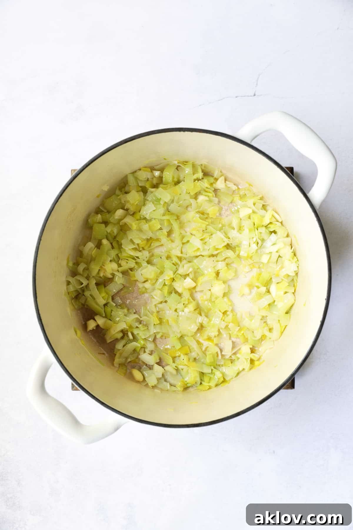 Gently cooked and softened leeks, glistening in butter and oil, nestled in a white enameled Dutch oven, forming the aromatic base of the soup.