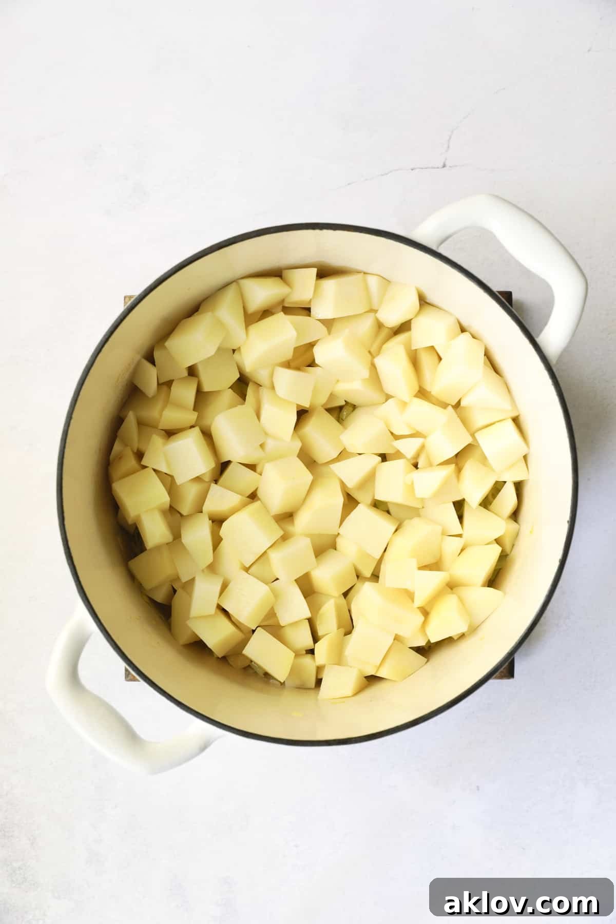 Comforting White Cheddar Potato Leek Soup 8 Photo of cubed potatoes in white Dutch oven.