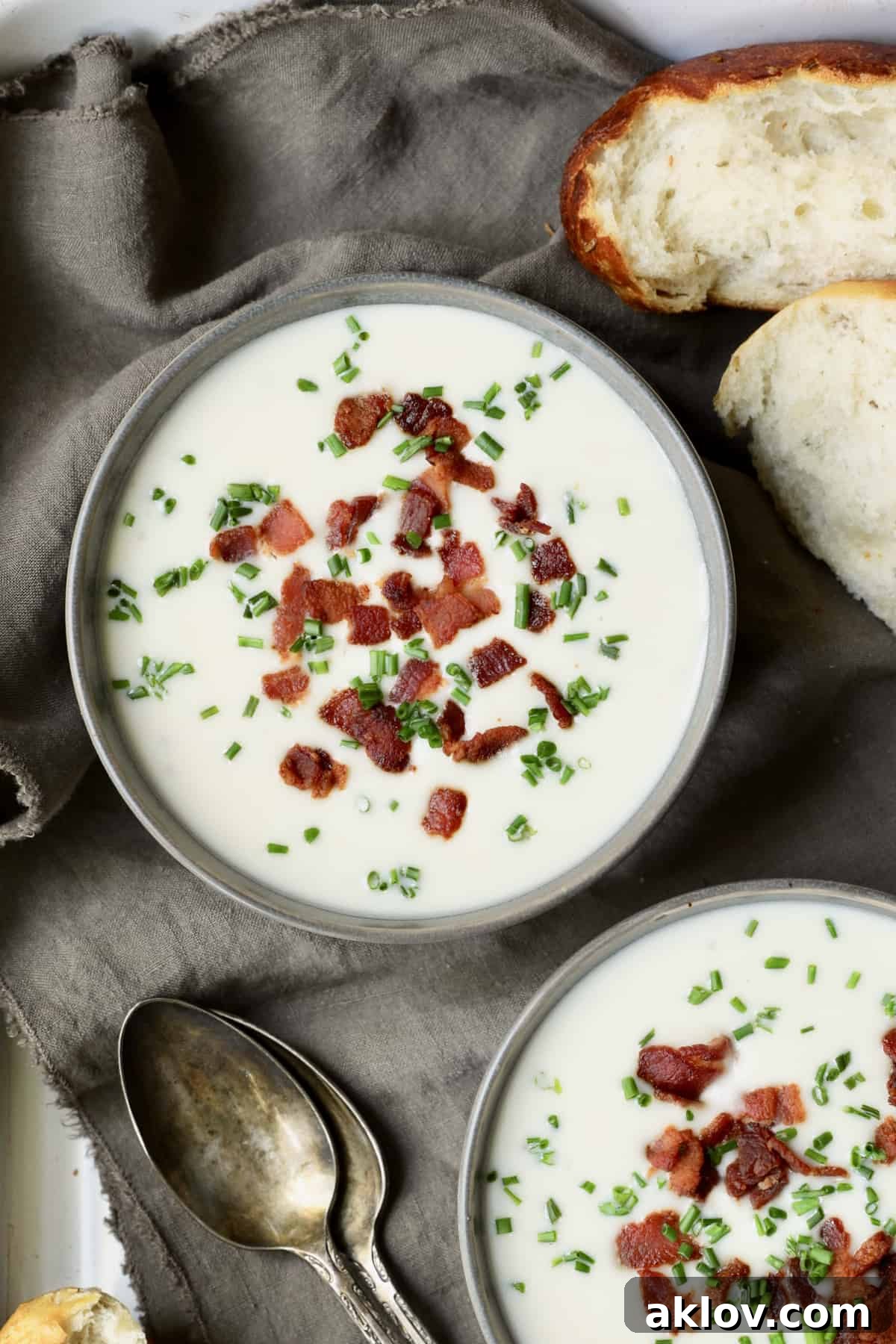 Comforting White Cheddar Potato Leek Soup 10 Close-up photo of Potato Leek Soup with White Cheddar in gray bowls garnished with bacon and chives.