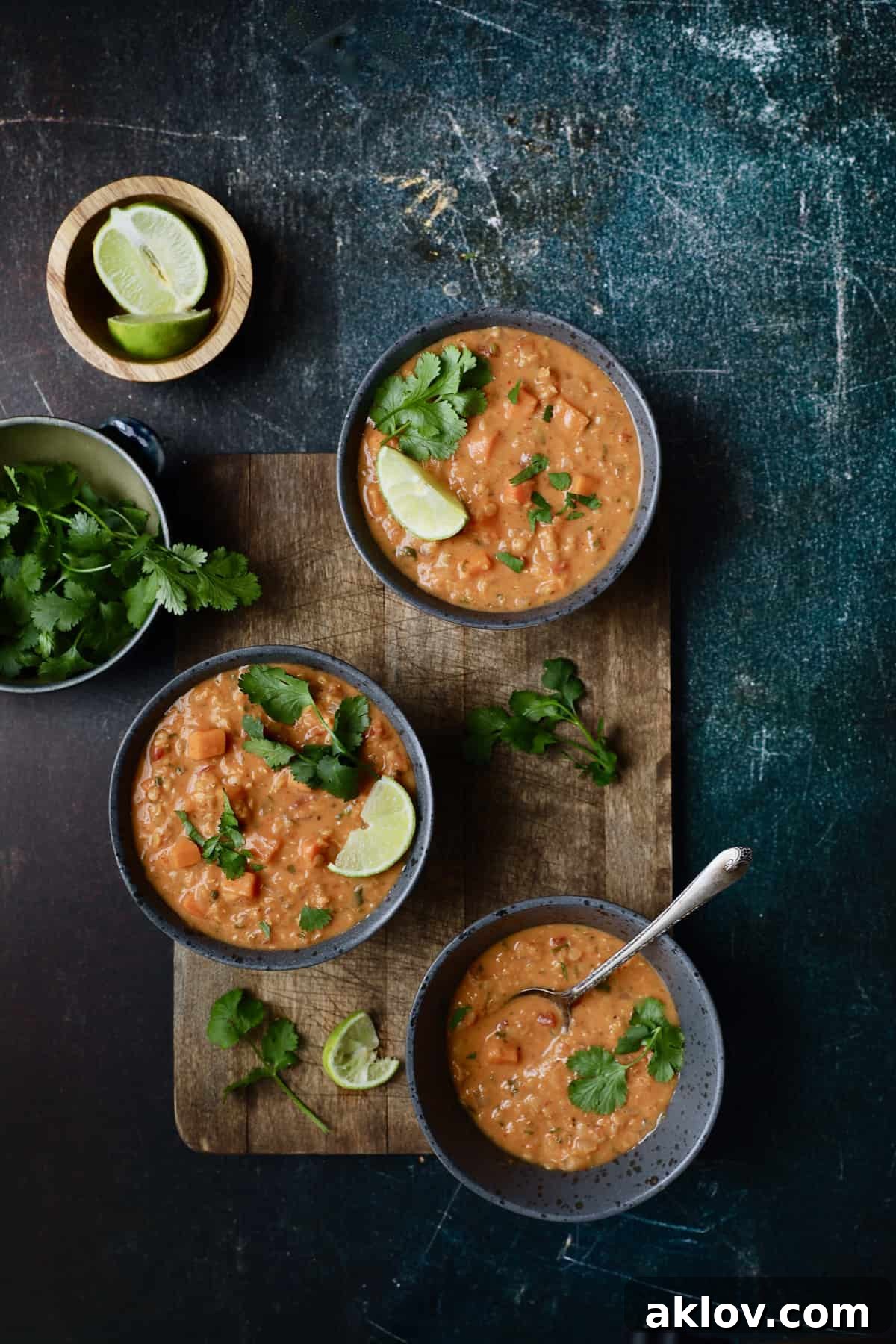 Photo of Thai Red Curry Sweet Potato and Lentil Soup garnished with lime and cilantro on a rustic blue background.