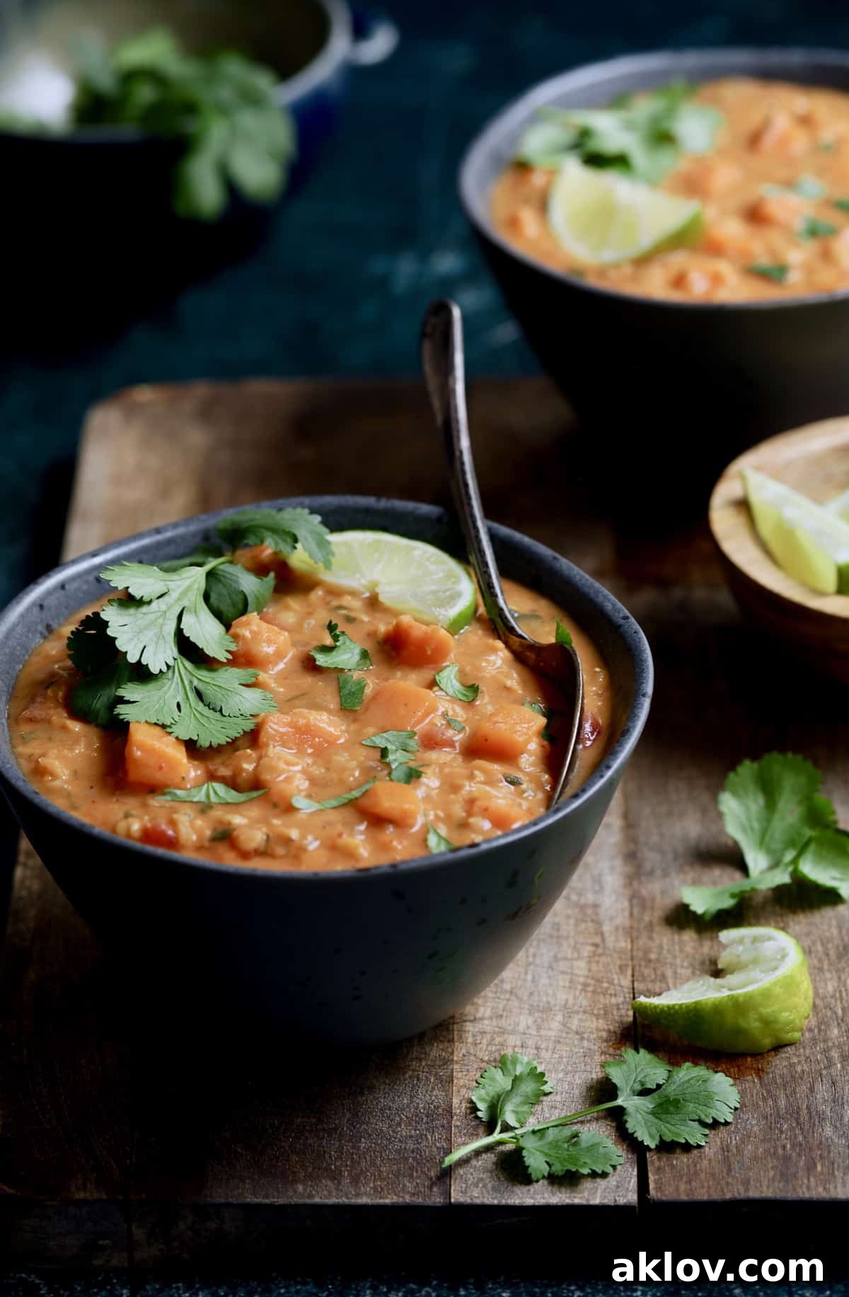 A single gray bowl of Thai Red Curry Sweet Potato and Lentil Soup, garnished with a lime wedge and cilantro sprigs, presented on a light wooden surface.
