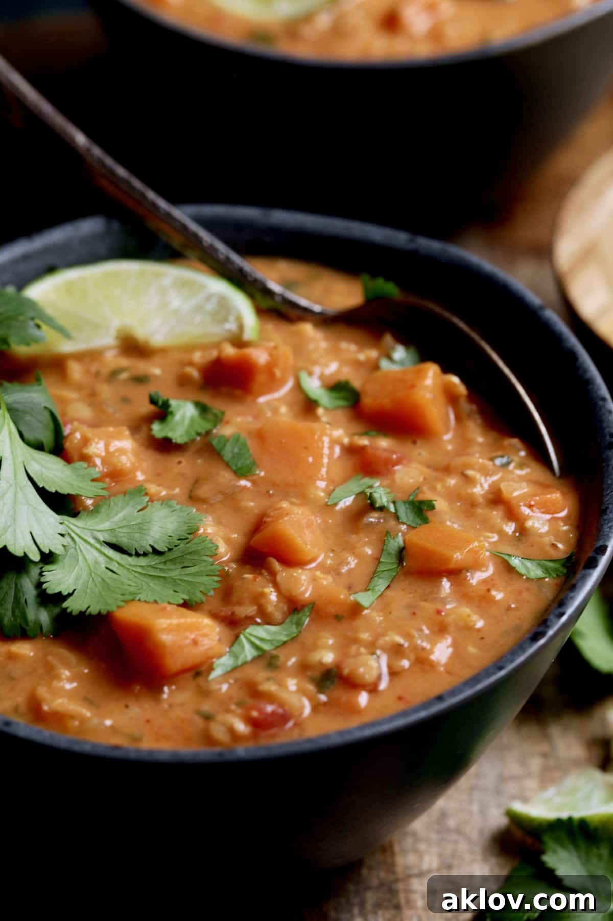 Close-up photo of Thai Red Curry Sweet Potato and Lentil Soup in a gray bowl, garnished with fresh lime and cilantro.