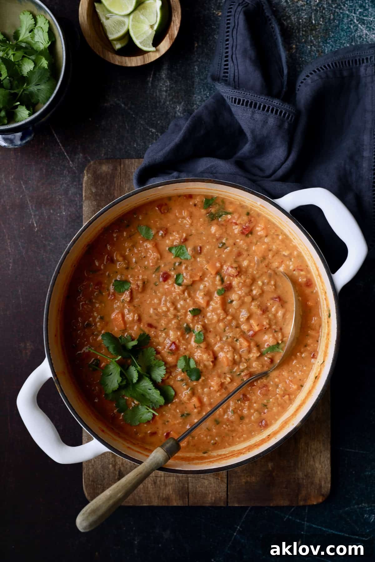 A white Dutch oven filled with simmering Thai Red Curry Sweet Potato and Lentil Soup, placed on a wooden cutting board. The steam rises gently, hinting at the warm, inviting aroma.
