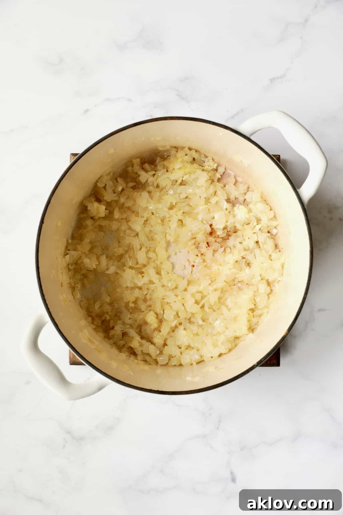 Process photo of onions cooking in white Dutch oven until soft and translucent.