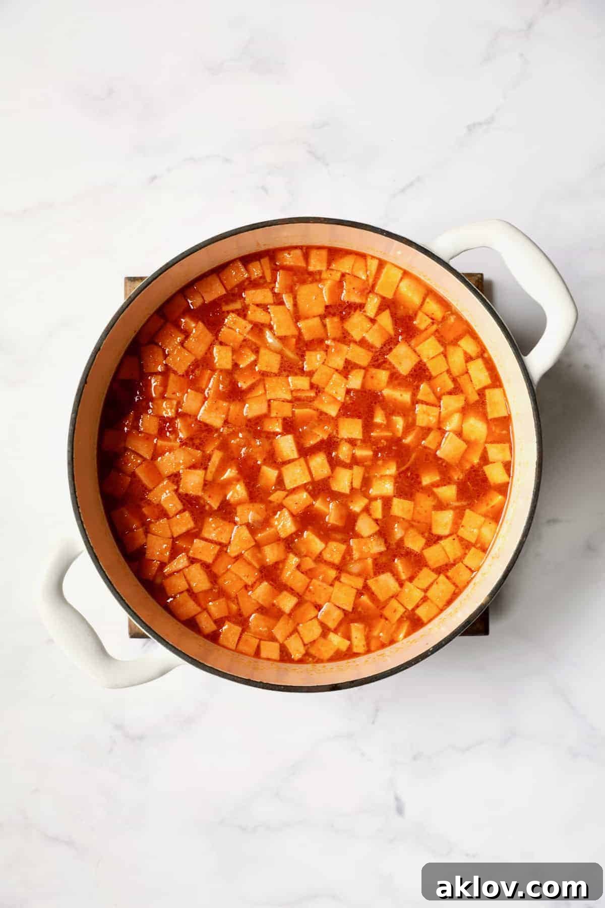 Process photo of Thai Red Curry Sweet Potato and Lentil Soup with vegetable broth, sweet potatoes, lentils, and diced tomatoes added to the Dutch oven, before simmering.