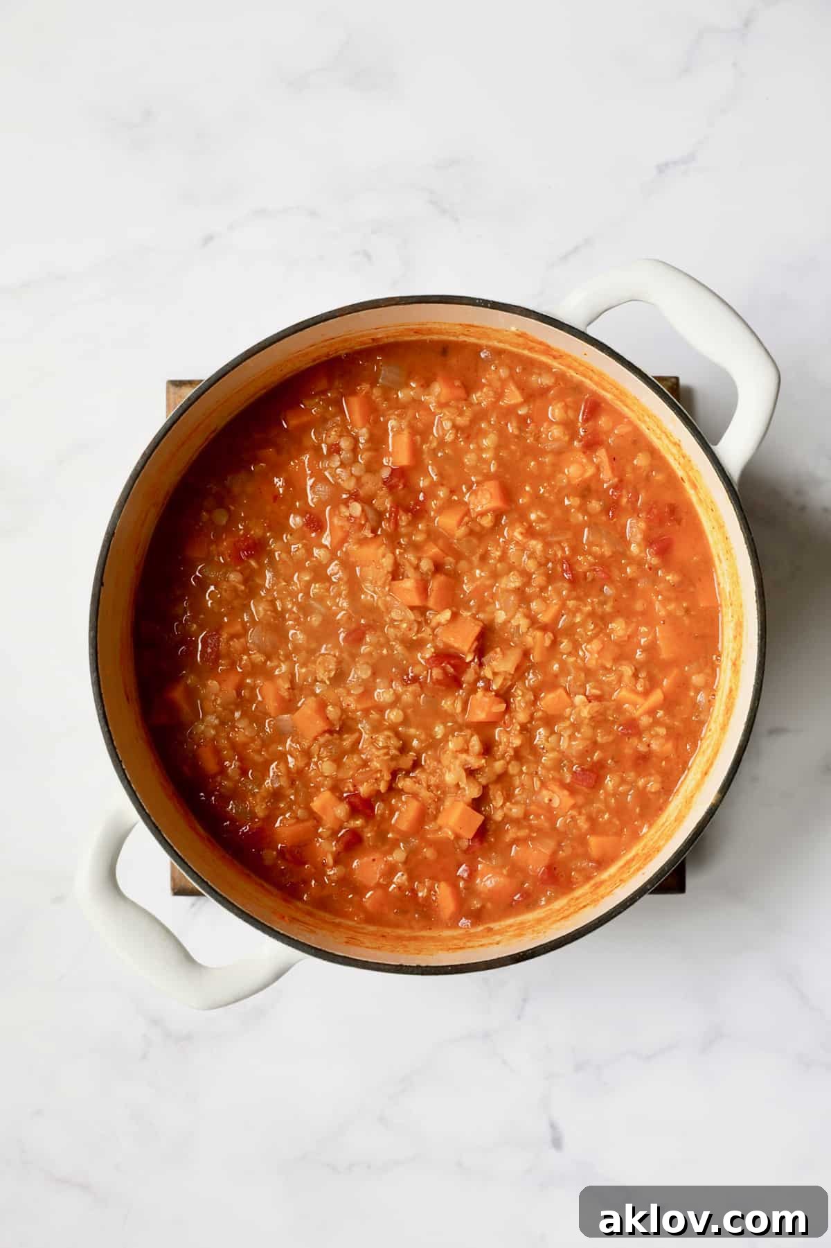Process photo of Thai Red Curry Sweet Potato and Lentil Soup simmering in a white Dutch oven, prior to the addition of coconut milk, showing tender vegetables and thickened broth.