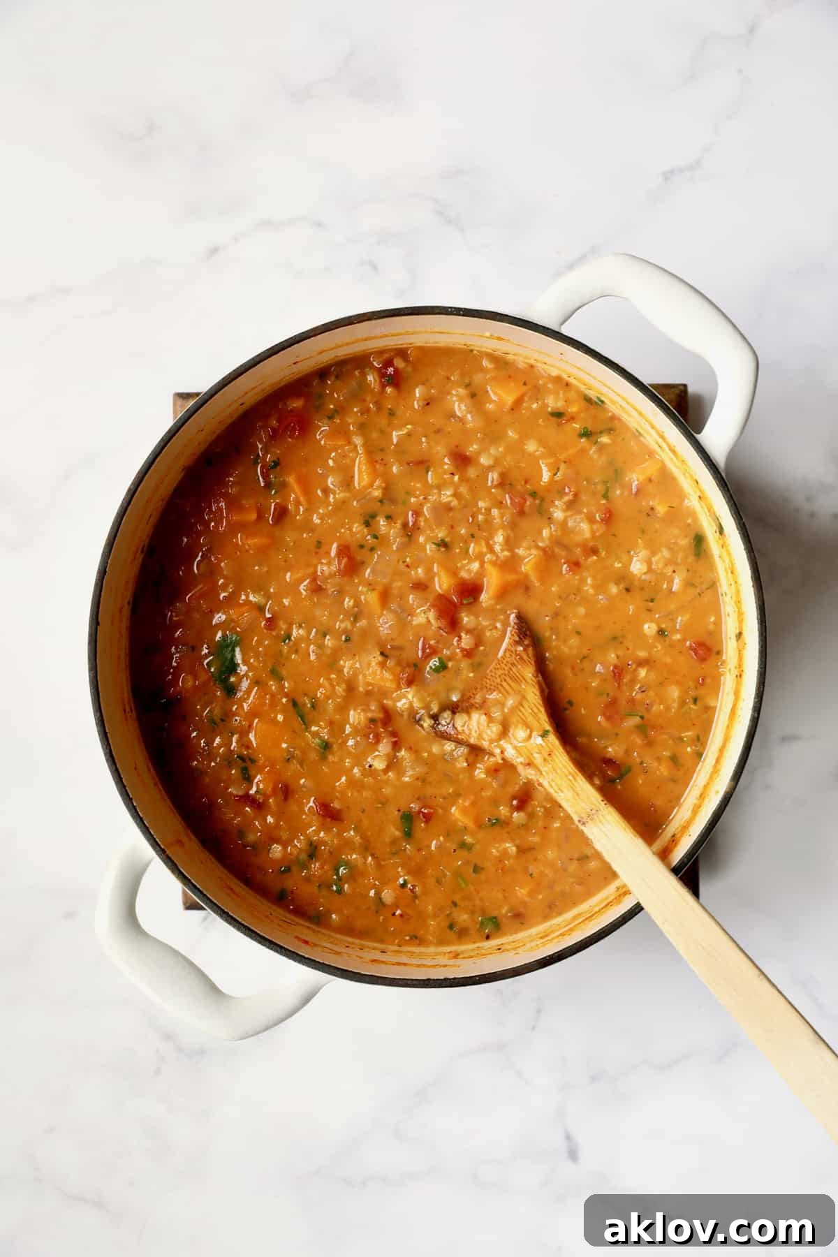 Process photo of Thai Red Curry Sweet Potato and Lentil Soup after coconut milk has been stirred in, creating a rich, creamy consistency in the white Dutch oven.