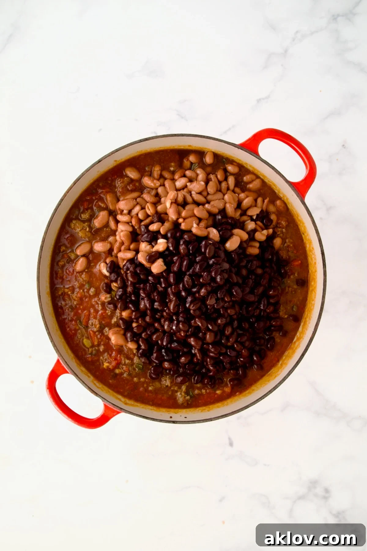 Beans added to chili in process in red Dutch oven.