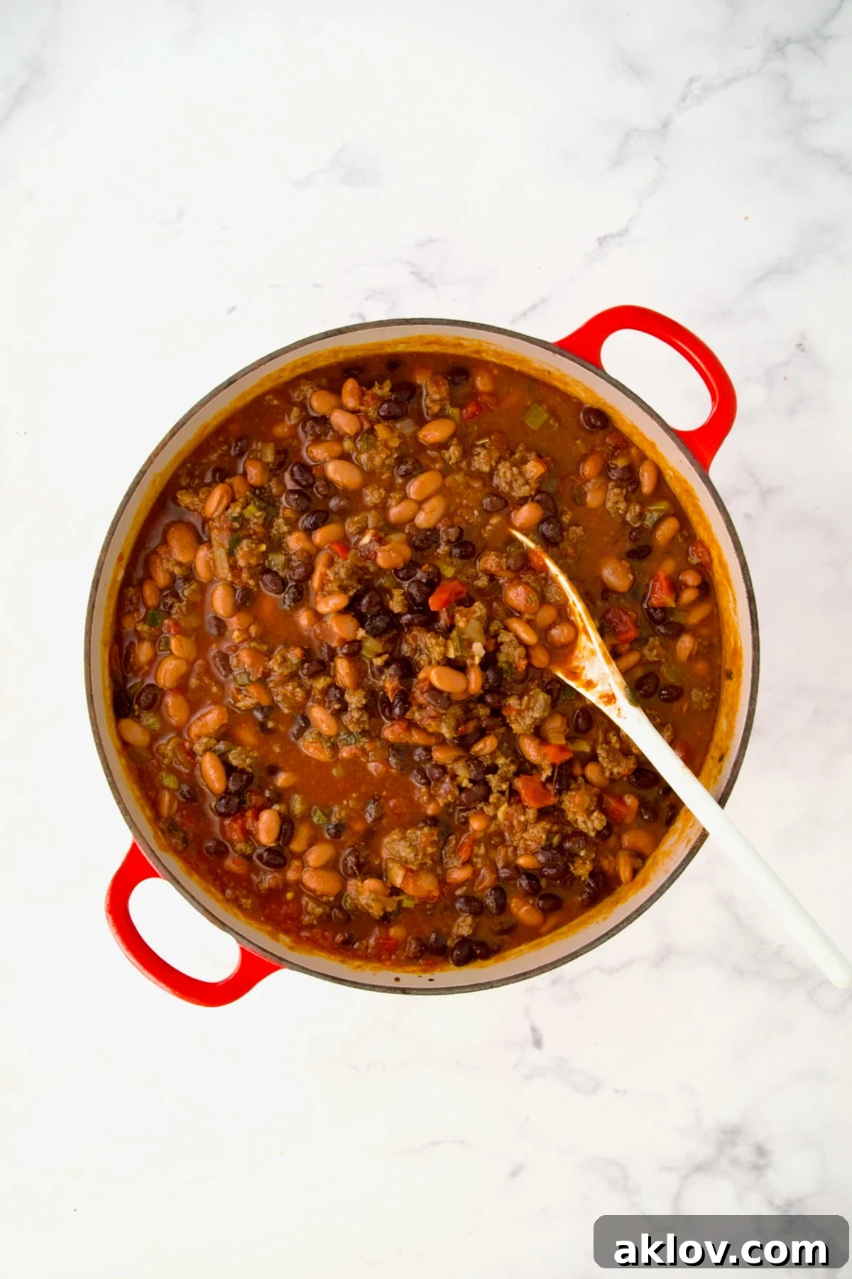 Beans stirred into chili in process in red Dutch oven.