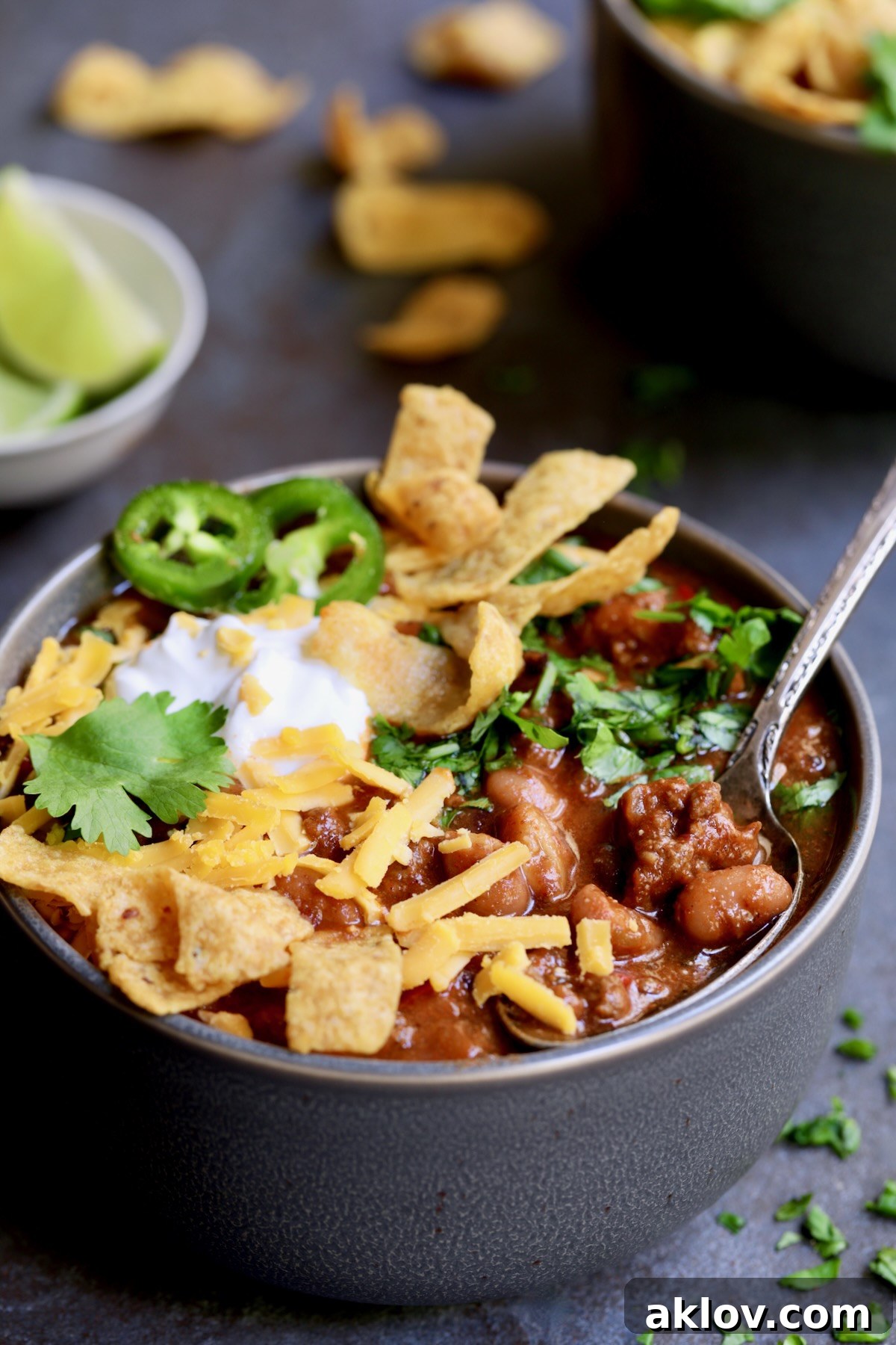 One bowl of Game Day Chili with corn chips, cheese, sour cream jalapeno slices and cilantro in gray bowl.