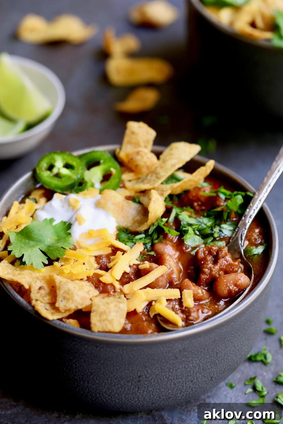 One bowl of Game Day Chili with corn chips, cheese, sour cream jalapeno slices and cilantro in gray bowl.