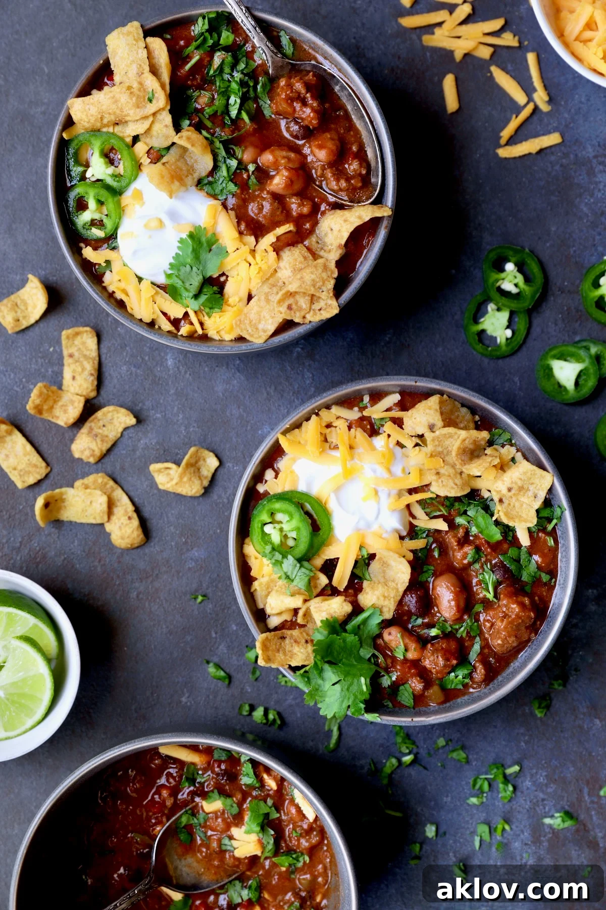 Two bowls of Game Day Chili with corn chips, cheese, sour cream jalapeno slices and cilantro in gray bowl.