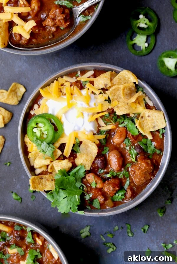 One bowl of Dutch Oven Chili with corn chips, cheese, sour cream jalapeno slices and cilantro in gray bowl.