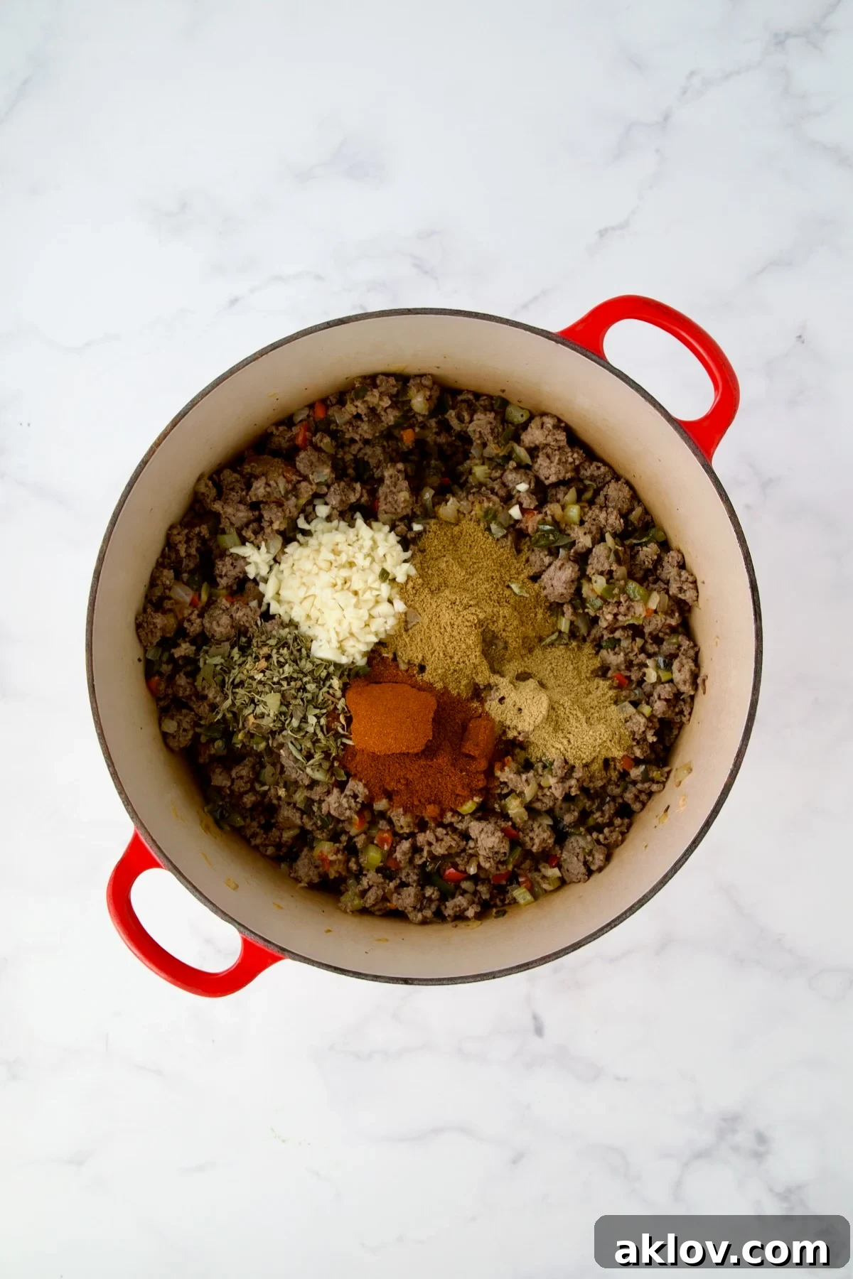 Spices added to ground beef and vegetables in red Dutch oven.