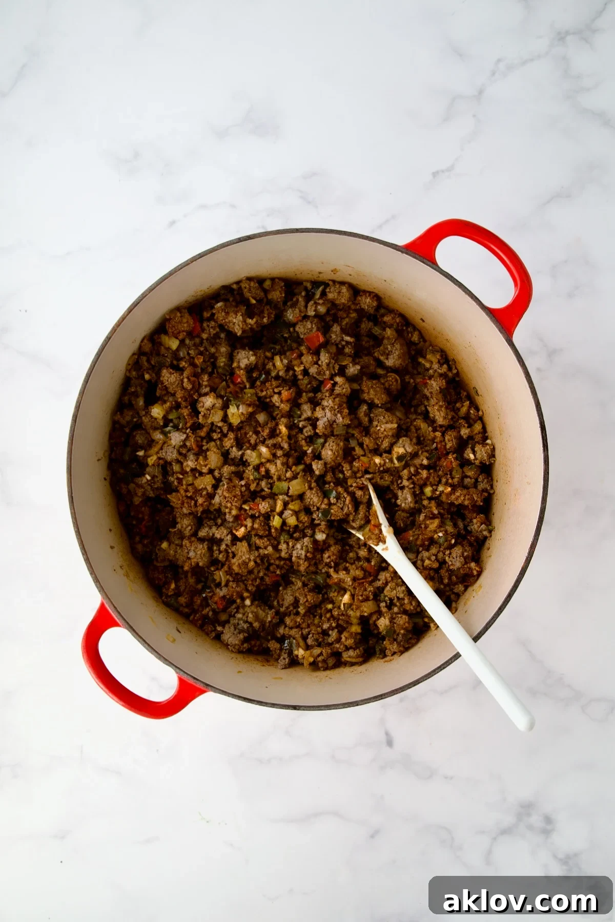 Spices stirred into ground beef and vegetables in red Dutch oven.