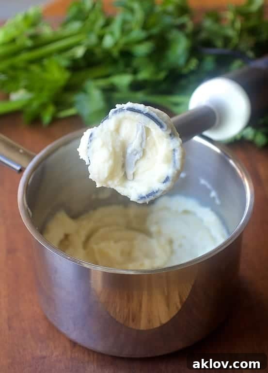 An immersion blender actively pureeing the cooked celery root mixture directly in a saucepan, demonstrating the easy process to achieve a smooth consistency.