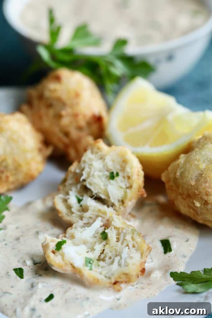 Close-up photo of a Crab and Artichoke Beignet cut open to reveal its tender interior, served with Jalapeno Remoulade and garnished with lemon and parsley.