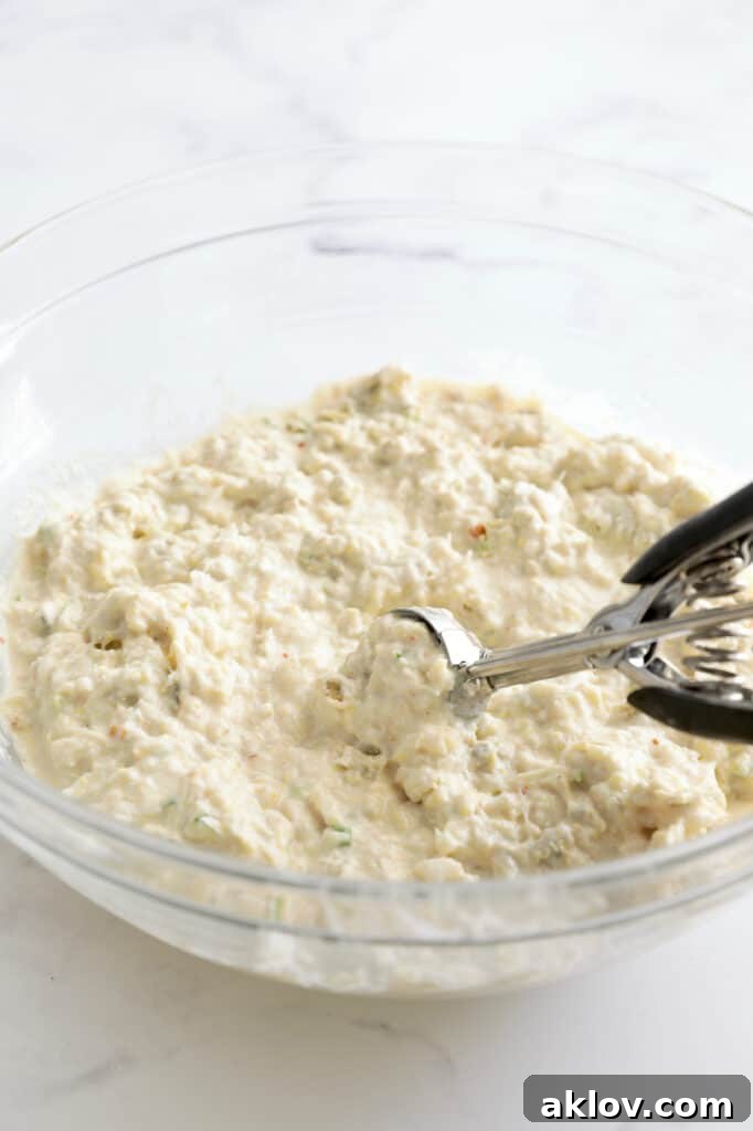 Photo of beignet batter being carefully scooped out from a glass bowl, ready for frying.