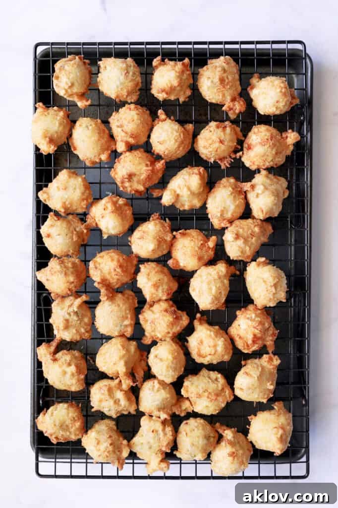 Photo of freshly fried Crab and Artichoke Beignets cooling on a wire rack over a rimmed baking sheet, ready to be served.
