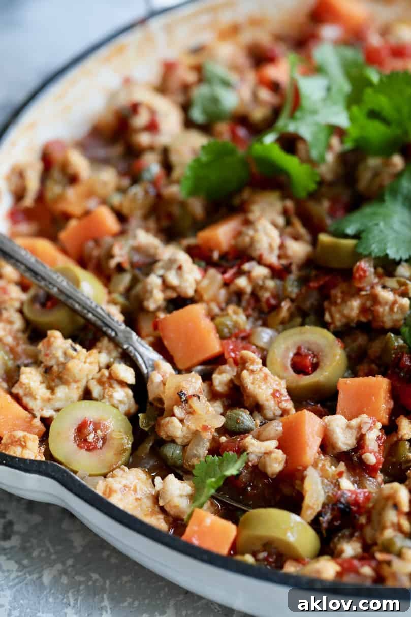 Close-up photo of Cuban-Style Turkey Picadillo with Sweet Potatoes in white skillet with spoon about to remove some.