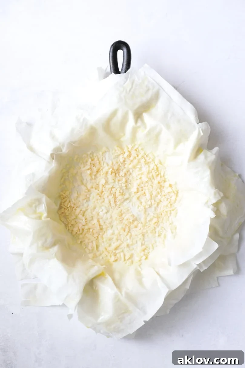 Skillet Spanakopita with Spinach and Feta 11 Photo of all phyllo dough layers in a cast iron skillet, topped with a generous layer of Parmesan cheese, ready for the spinach filling. This image highlights the moisture barrier step.
