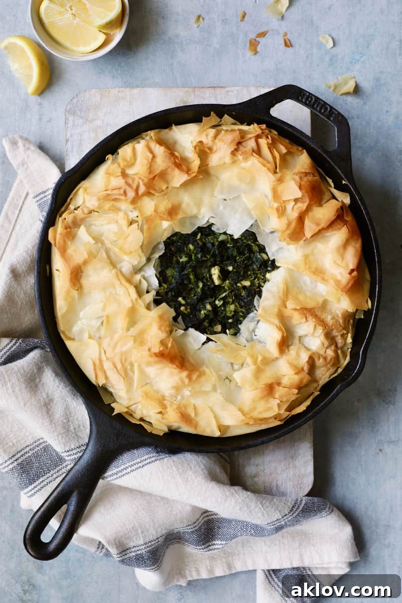 Skillet Spanakopita with Spinach and Feta 14 Photo of a baked Skillet Spanakopita (Greek Spinach and Feta Pie) on a cutting board, accompanied by a gray striped towel. The pie is golden and looks perfectly cooked.