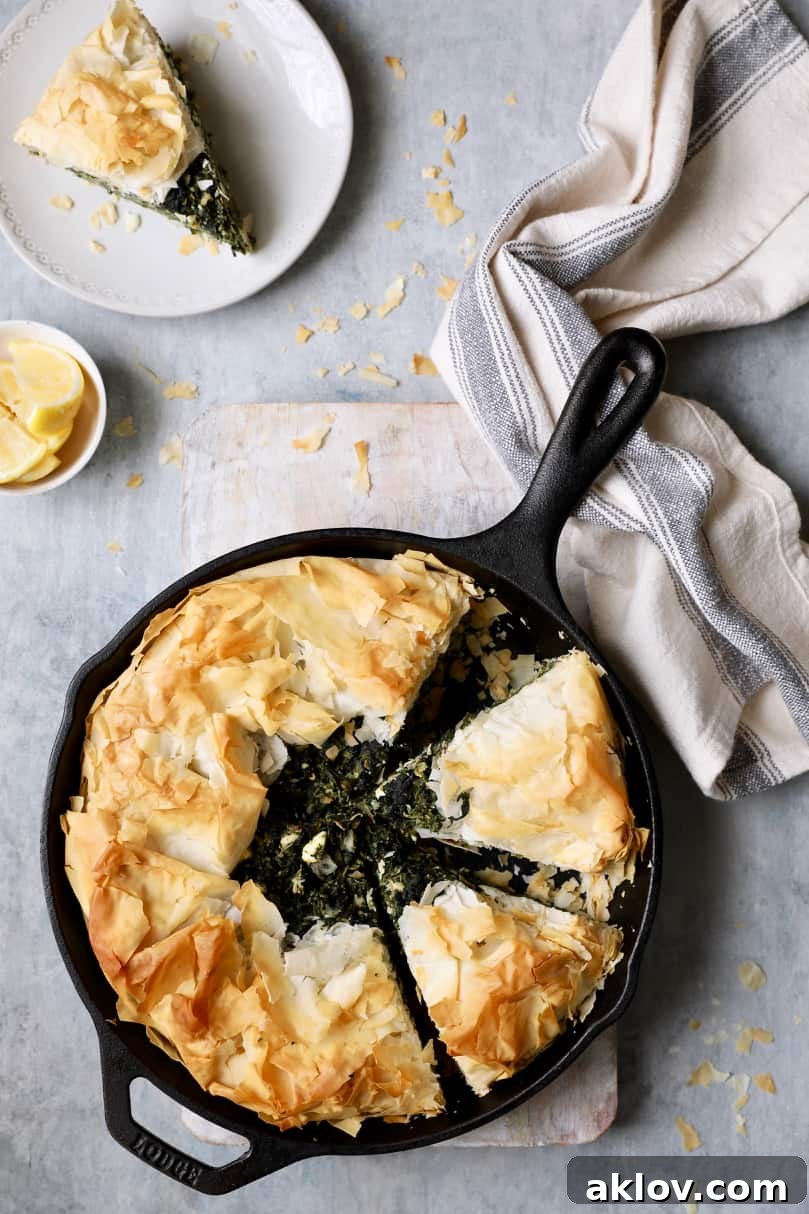 Skillet Spanakopita with Spinach and Feta 15 Photo of baked spanakopita on a light gray background with a slice cut and placed on a white plate. This showcases the pie ready for serving.