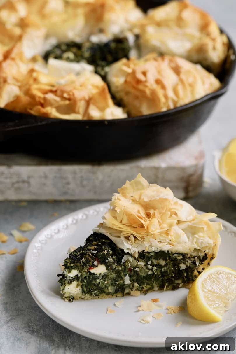Skillet Spanakopita with Spinach and Feta 16 Photo of one slice of Skillet Spanakopita (Greek Spinach and Feta Pie) on a small white plate with the rest of the pie in the background. This close-up highlights the texture and deliciousness.