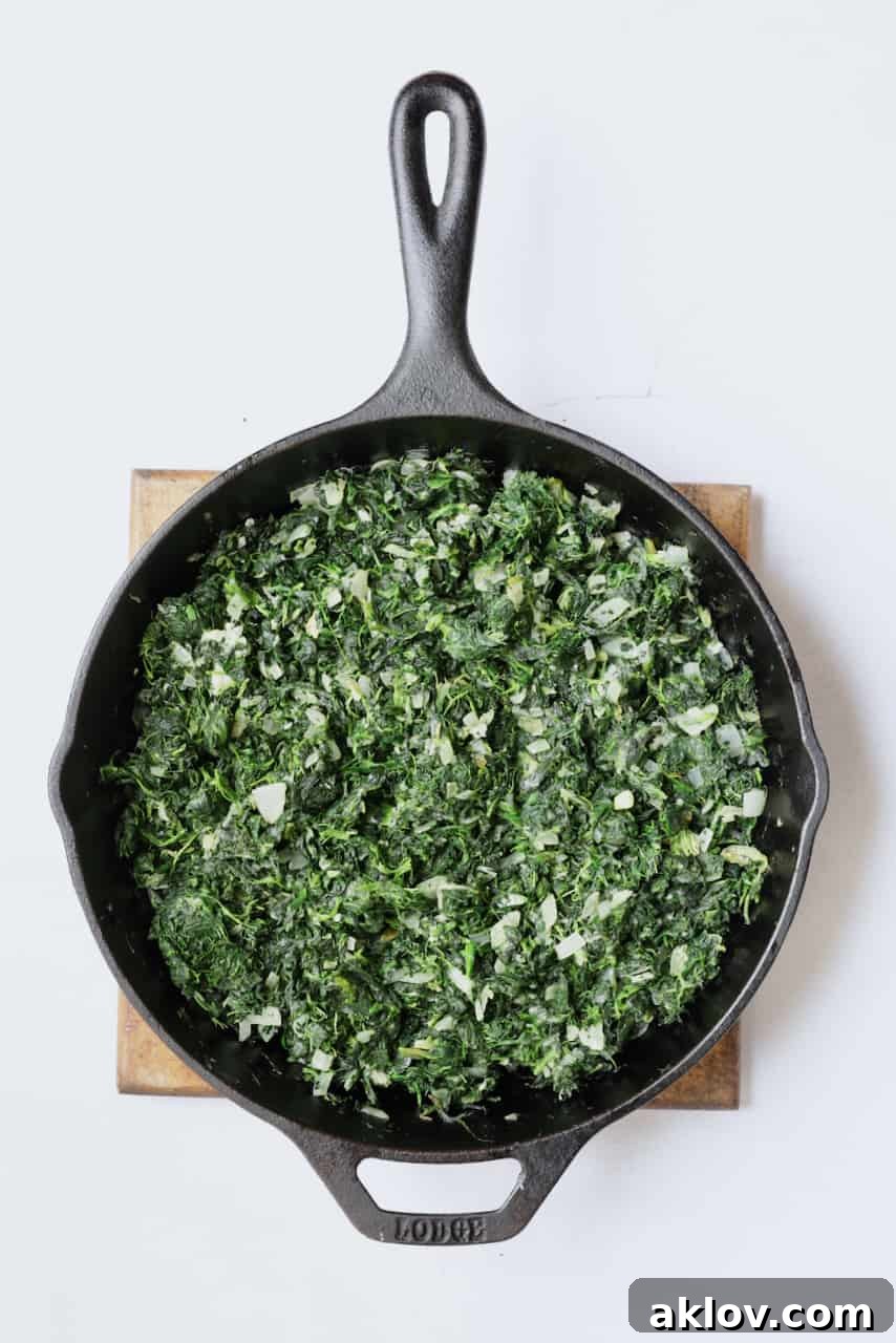 Skillet Spanakopita with Spinach and Feta 6 Photo of spinach and onions being cooked in a cast iron skillet. The vibrant green of the spinach contrasts beautifully with the translucent onions.