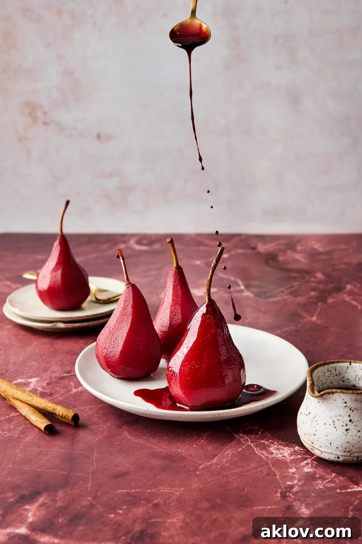 Three poached pears on white plate being drizzled with sauce.