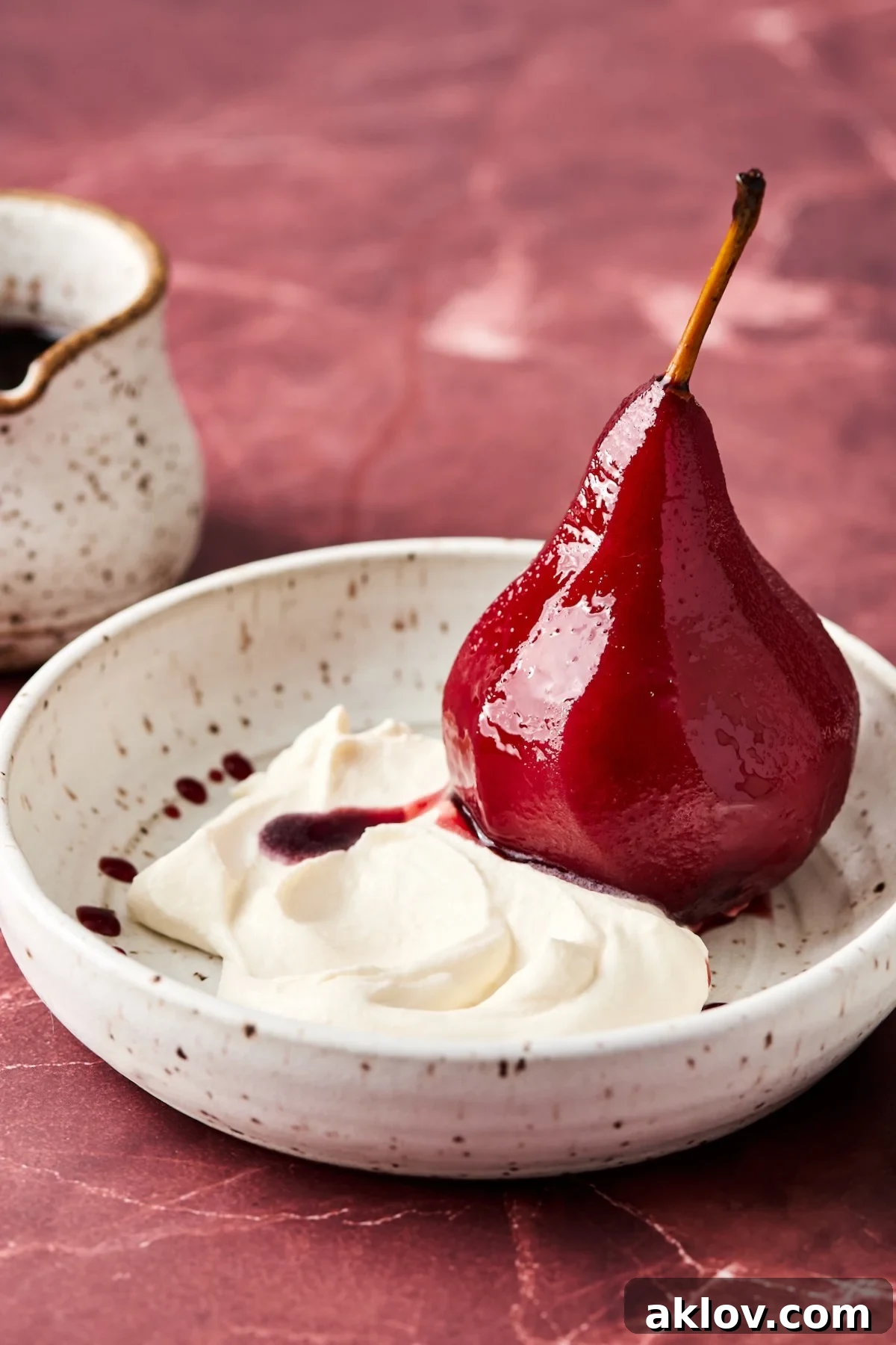 Poached pear sliced in half in bowl with Mascarpone Whipped Cream.