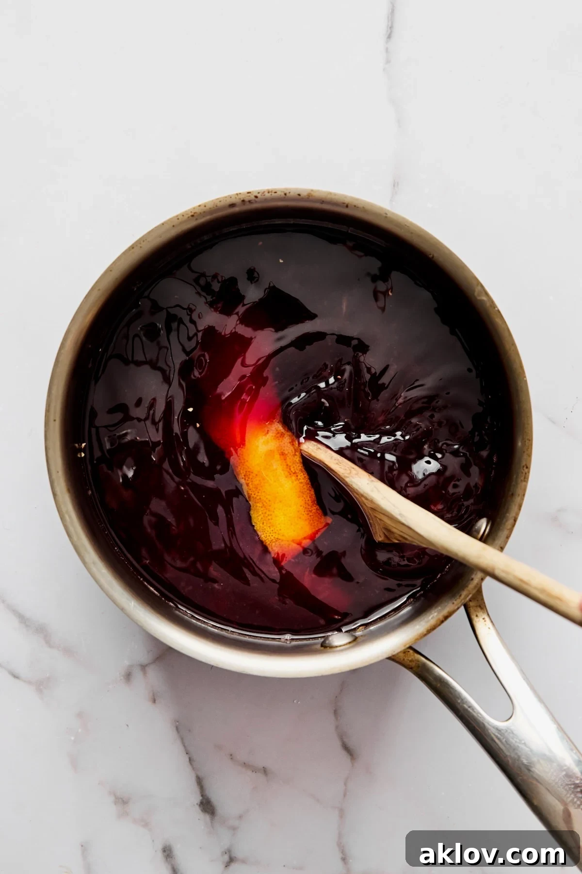 Red wine sauce in stainless steel sauce pan being mixed with wooden spoon.