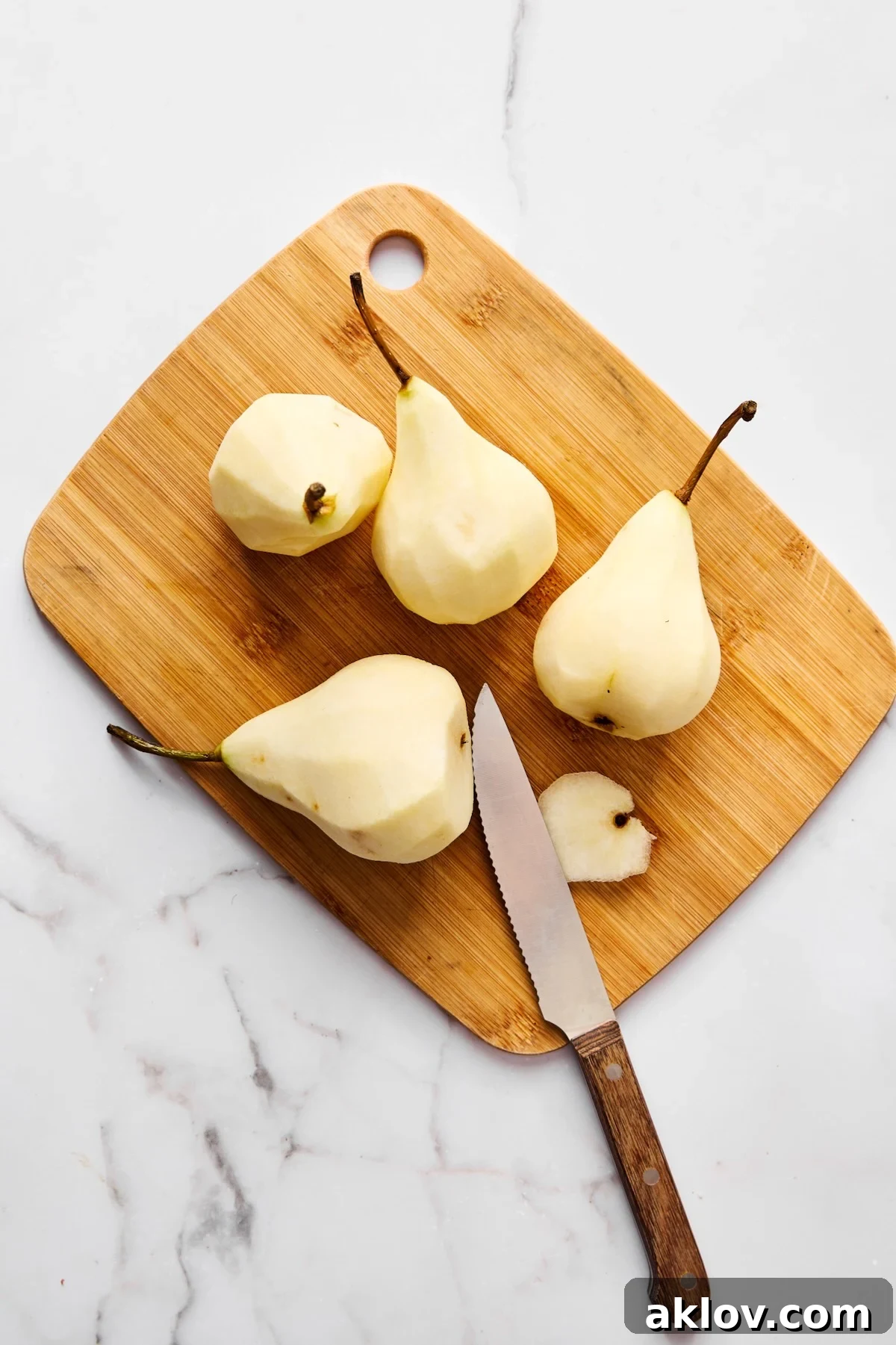 Four peeled pears with knife on wood cutting board.