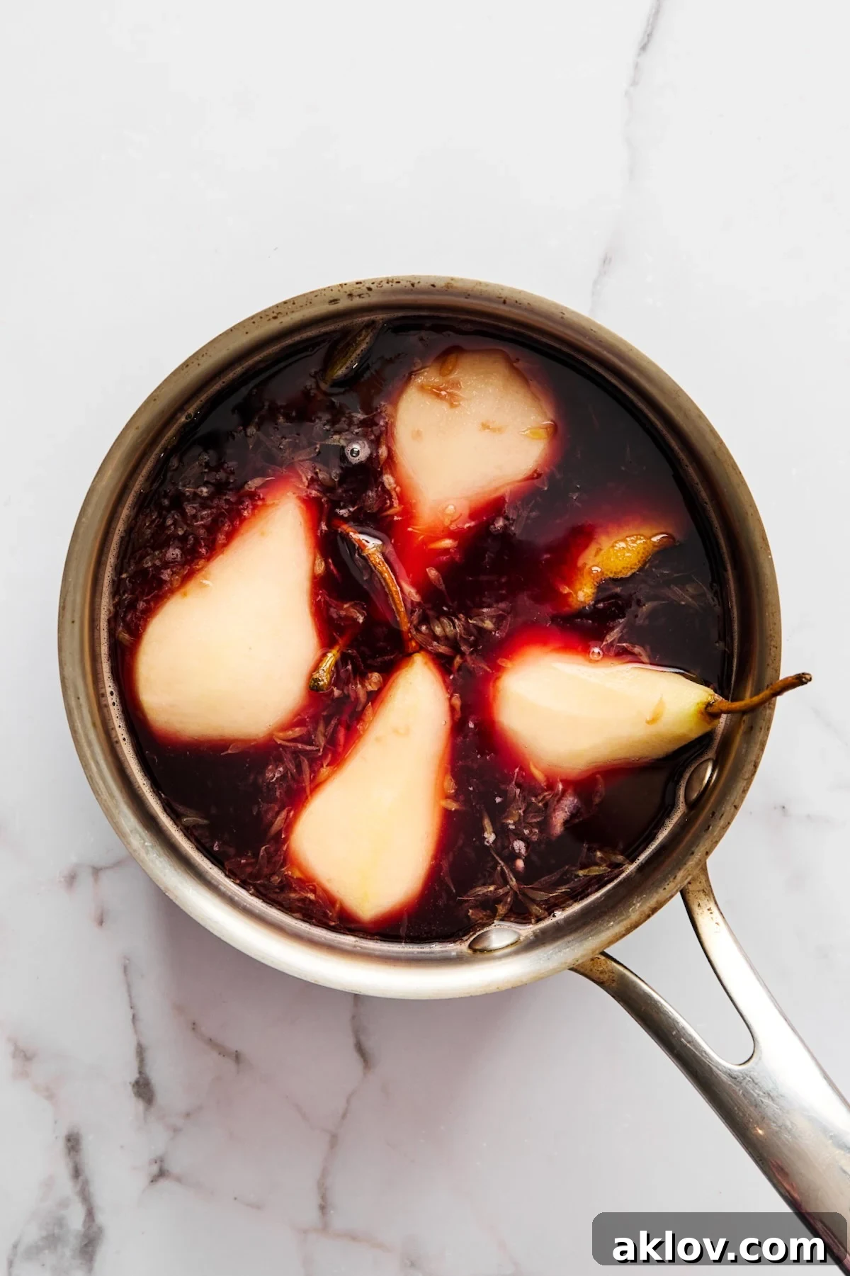 Four pears in stainless steel saucepan being simmered in red wine sauce.