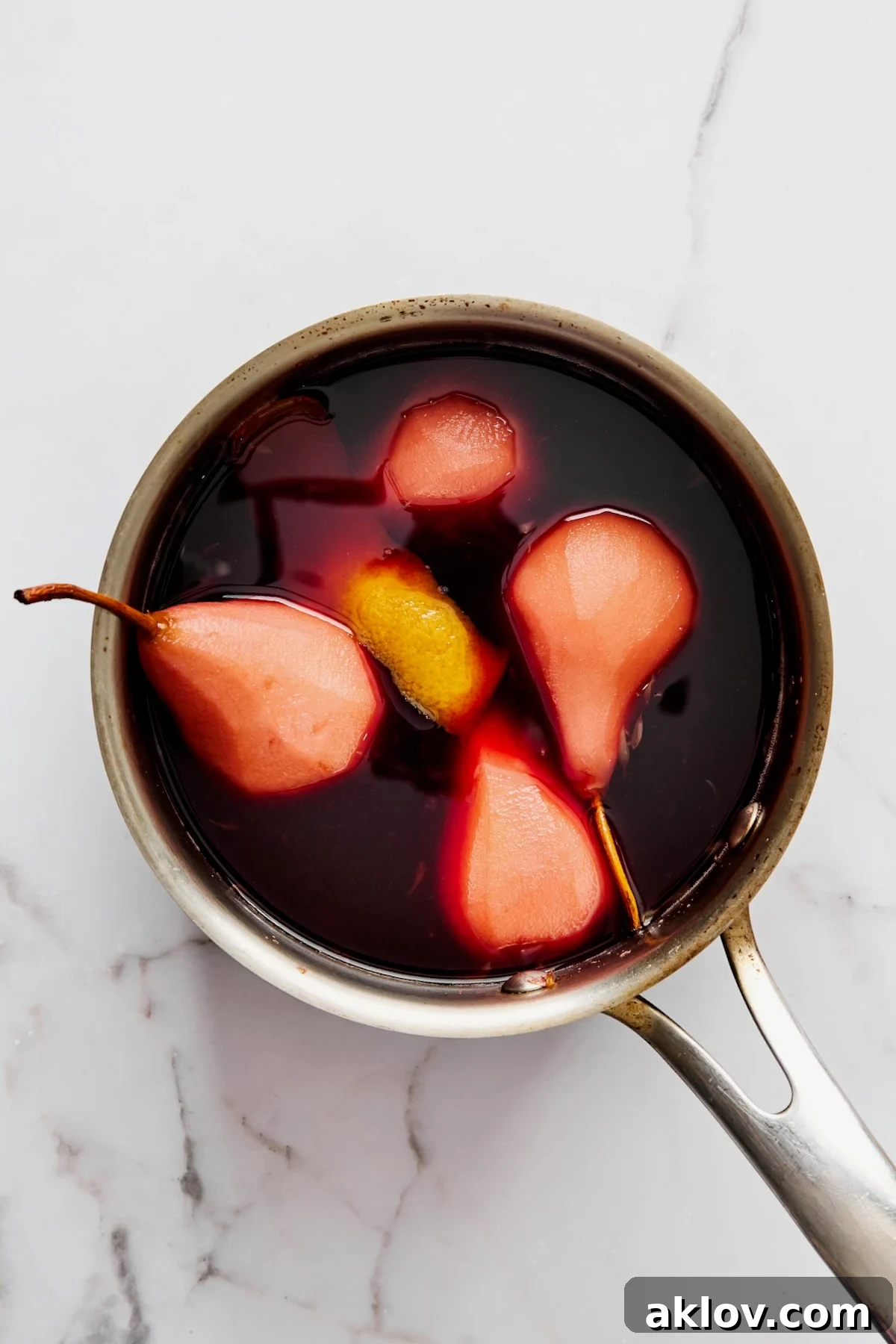 Four simmered pears in red wine sauce in stainless steel saucepan.