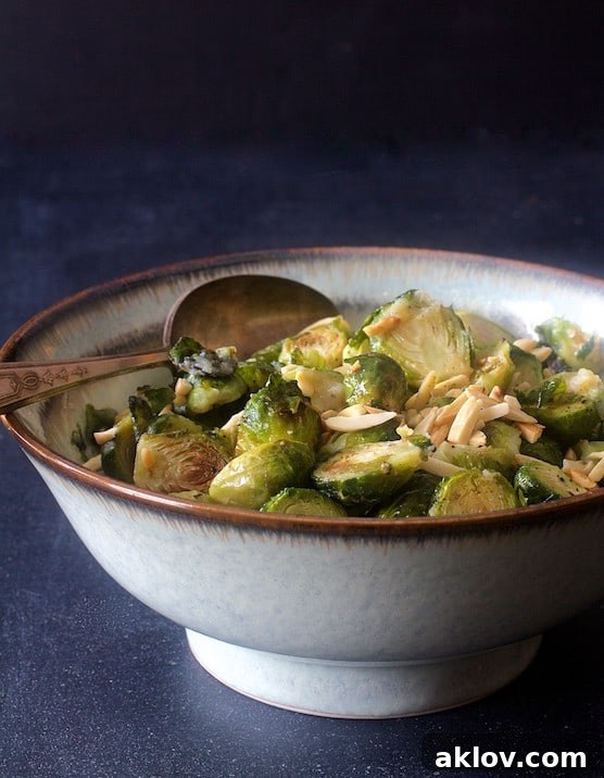 Photo of Roasted Brussels Sprouts with Browned Butter and Almonds in serving bowl with serving spoon on dark blue background.