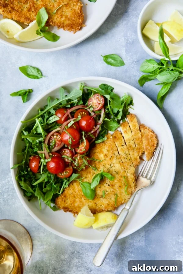 Chicken Milanese with Arugula and Cherry Tomato Salad garnished with fresh basil sprigs and lemon wedges.