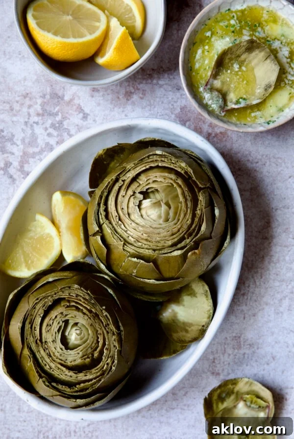 Instant Pot Artichokes (With Garlic Butter) in white oval serving bowl with lemon wedges.