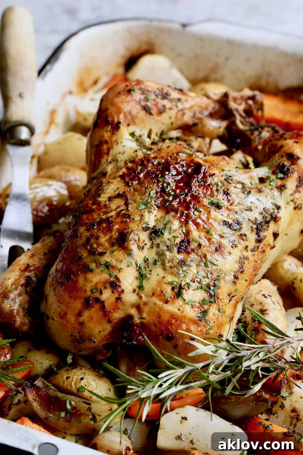 Photo of a perfectly roasted Garlic Herb Butter Roast Chicken with Root Vegetables, with a carving fork nearby, ready to be served, highlighting its succulent appearance.