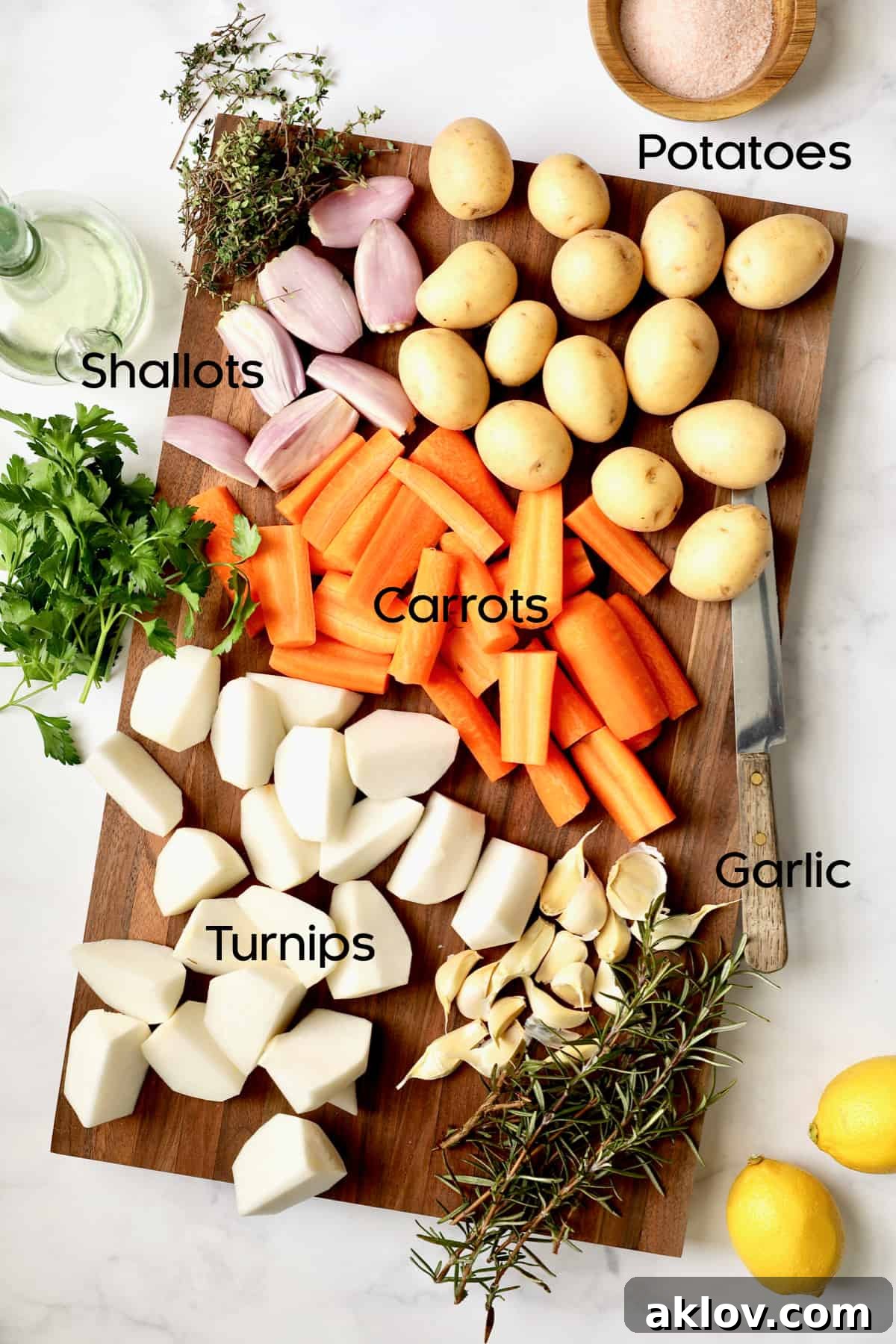 Photo of prepped root vegetables on wood cutting board, including potatoes, carrots, turnips, and shallots, cut and ready for roasting.