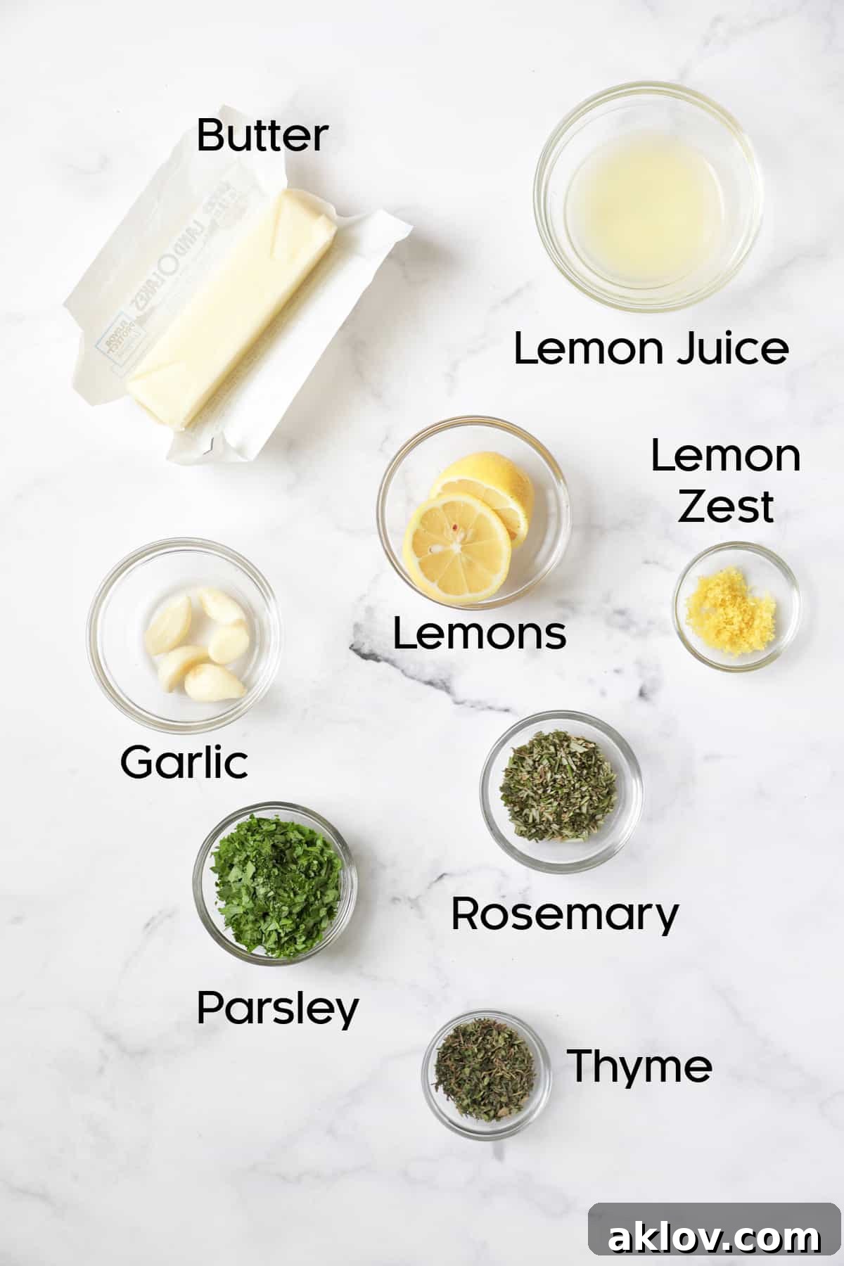 Ingredients for garlic herb butter in glass bowls on marble background, showing vibrant fresh herbs, zested lemon, minced garlic, and softened unsalted butter.