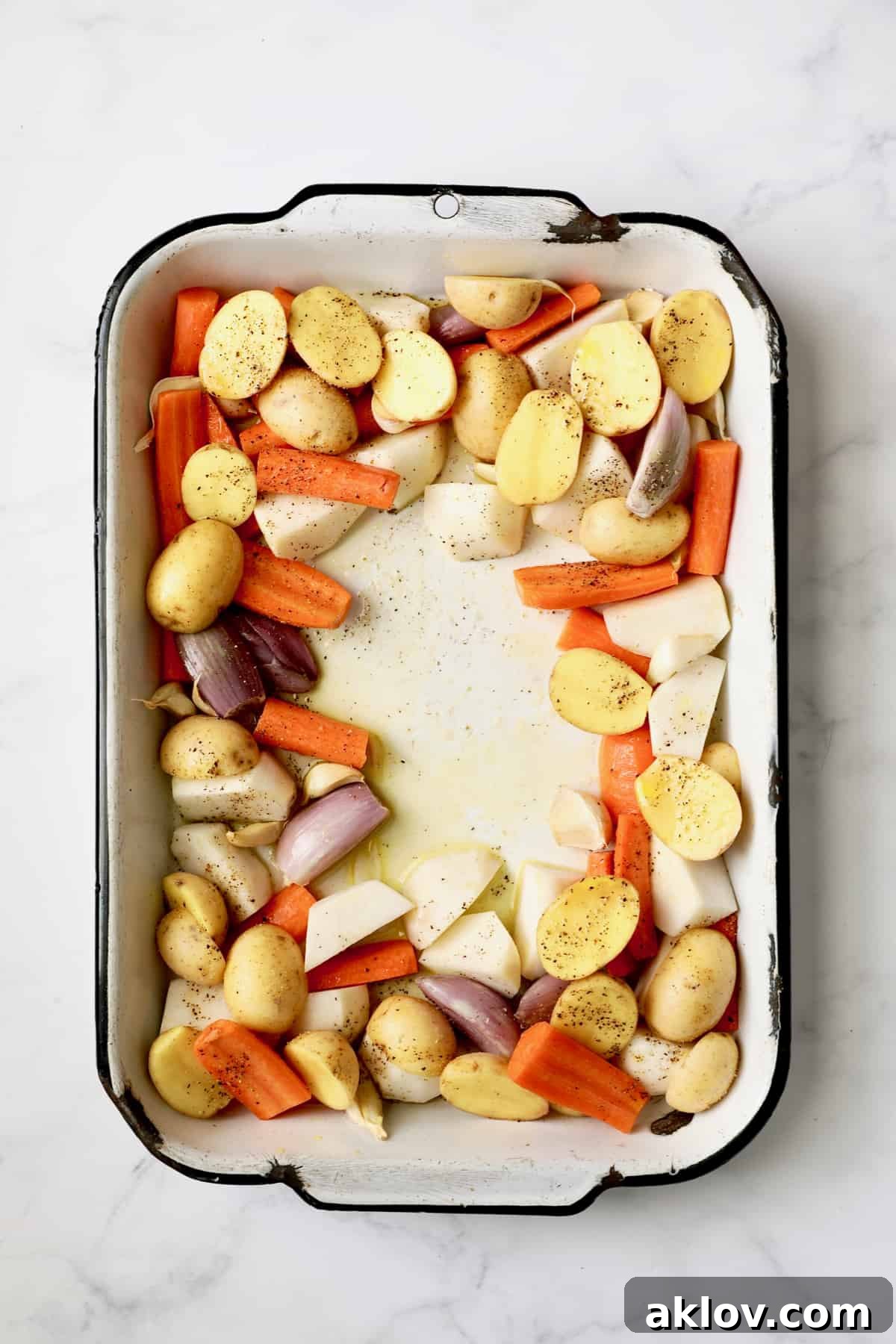 Photo of uncooked root vegetables in white roasting pan, seasoned and ready for the chicken, showing their vibrant colors and uniform cuts.