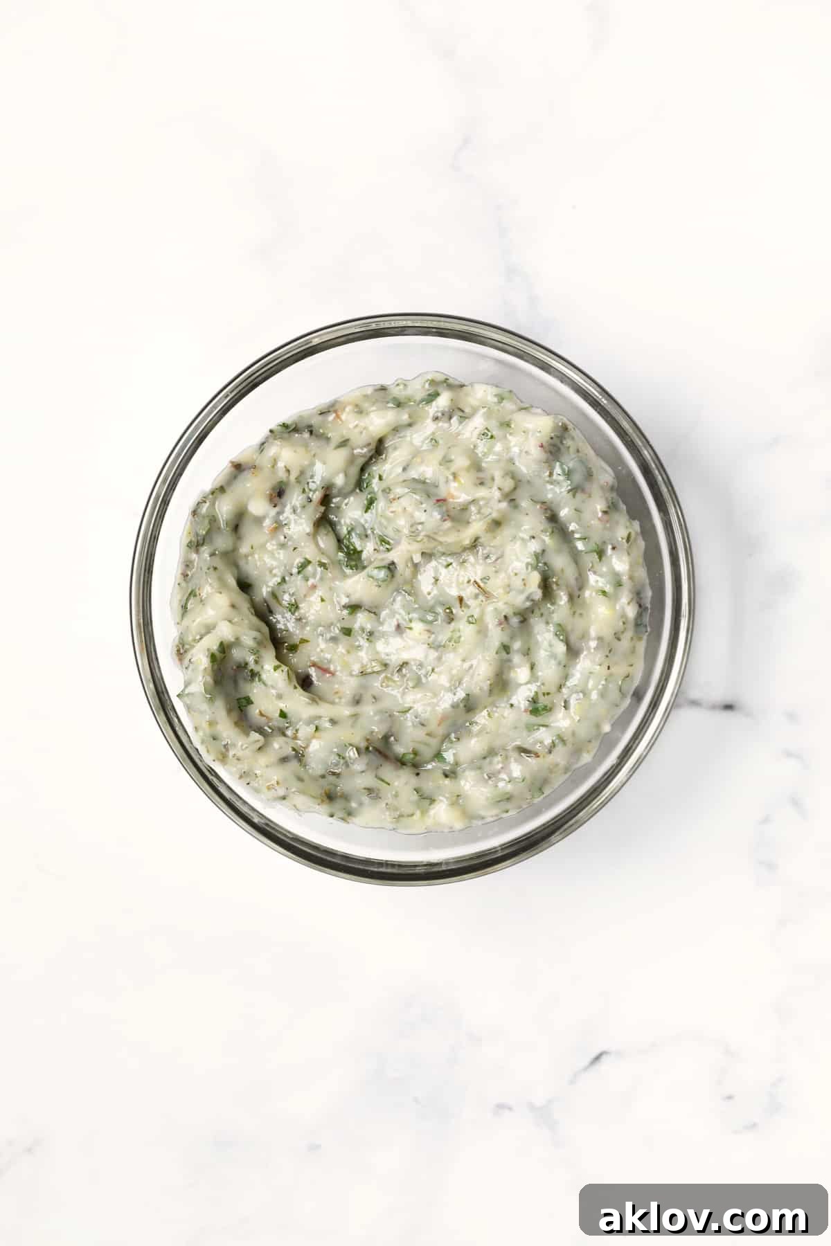 Photo of Garlic Herb Butter in glass bowl on white background, showing its vibrant color and smooth texture, ready to be applied.