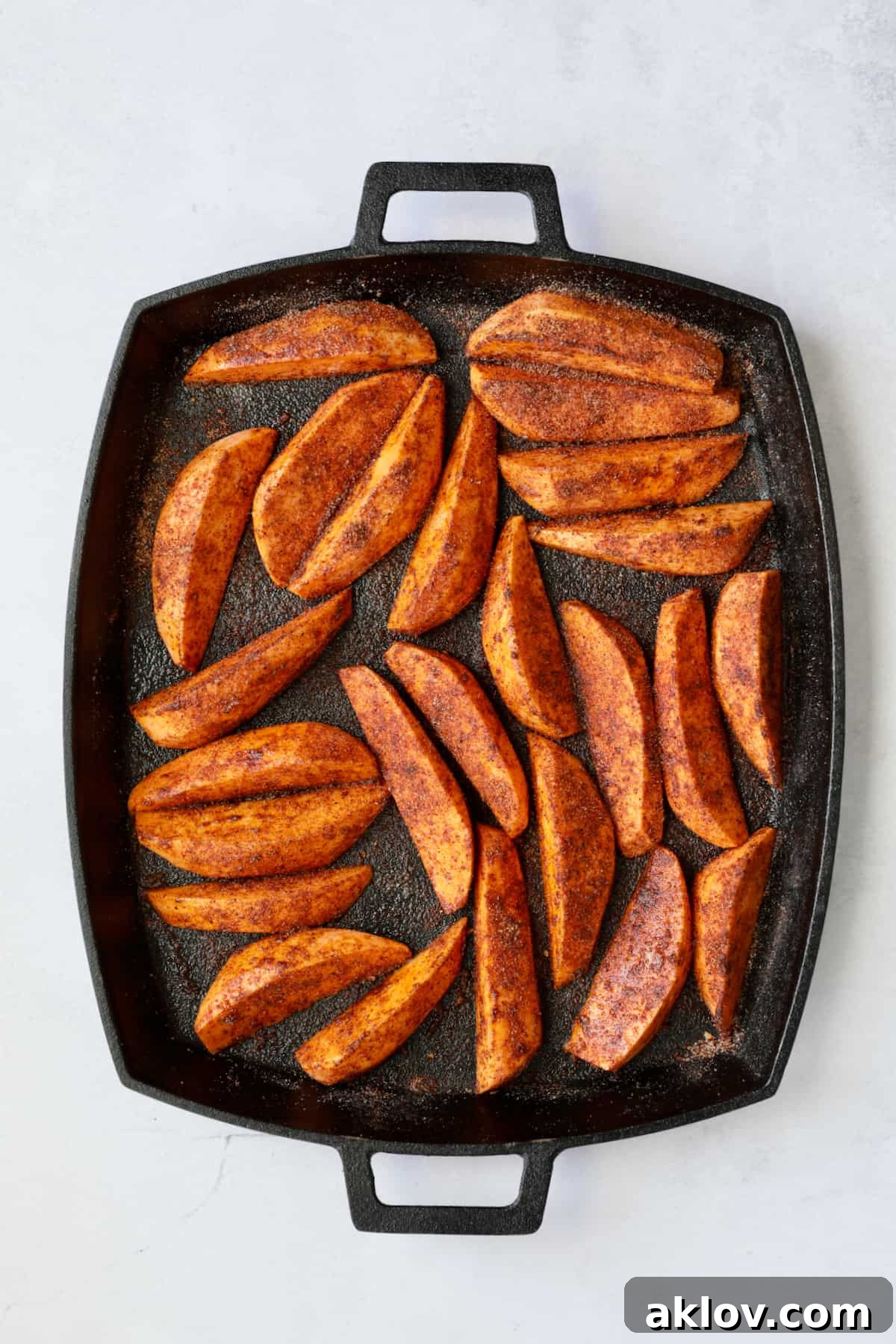 Southwestern Sweet Potato Wedges on cast iron pan with seasoning mix before being roasted.